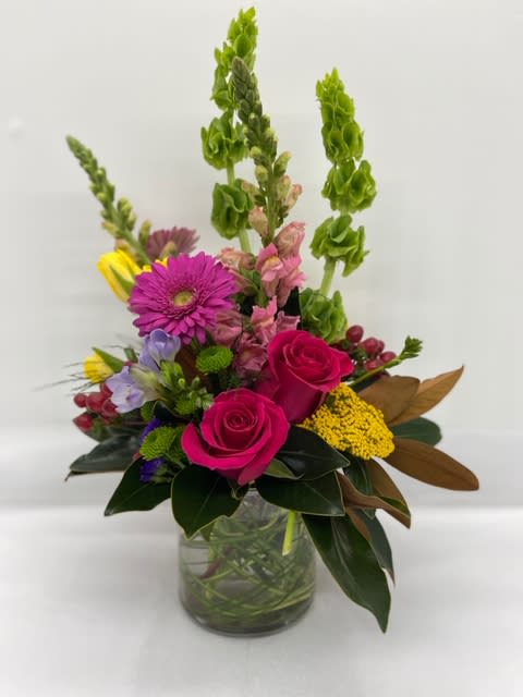 Mixed bouquet with pink roses, purple daisies, and tall green spikes in a glass vase