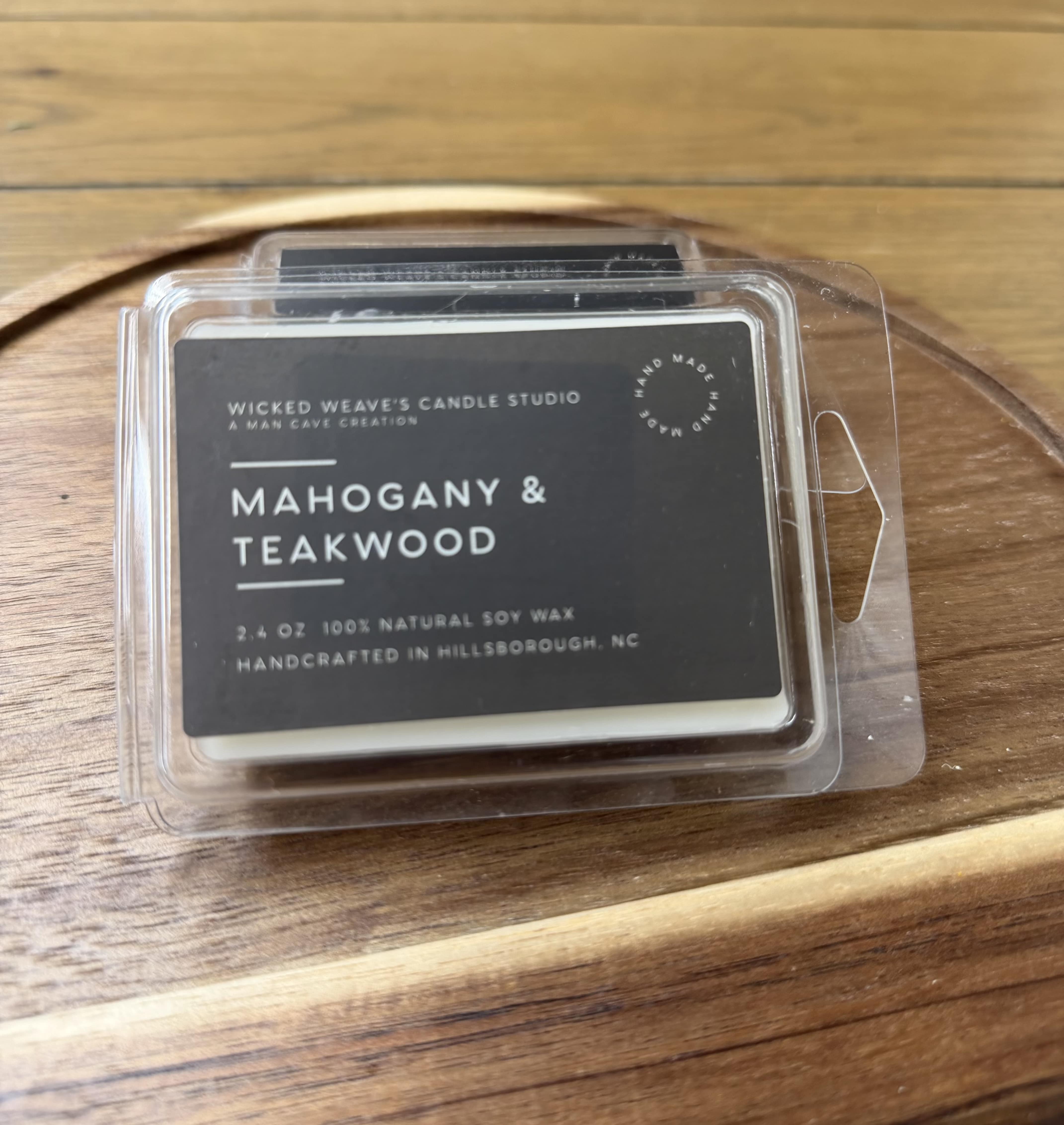 Clamshell candle package labeled Mahogany &amp; Teakwood on a wooden tray