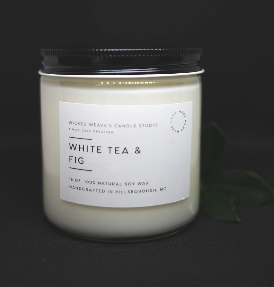 White candle in a glass jar with a black lid and label