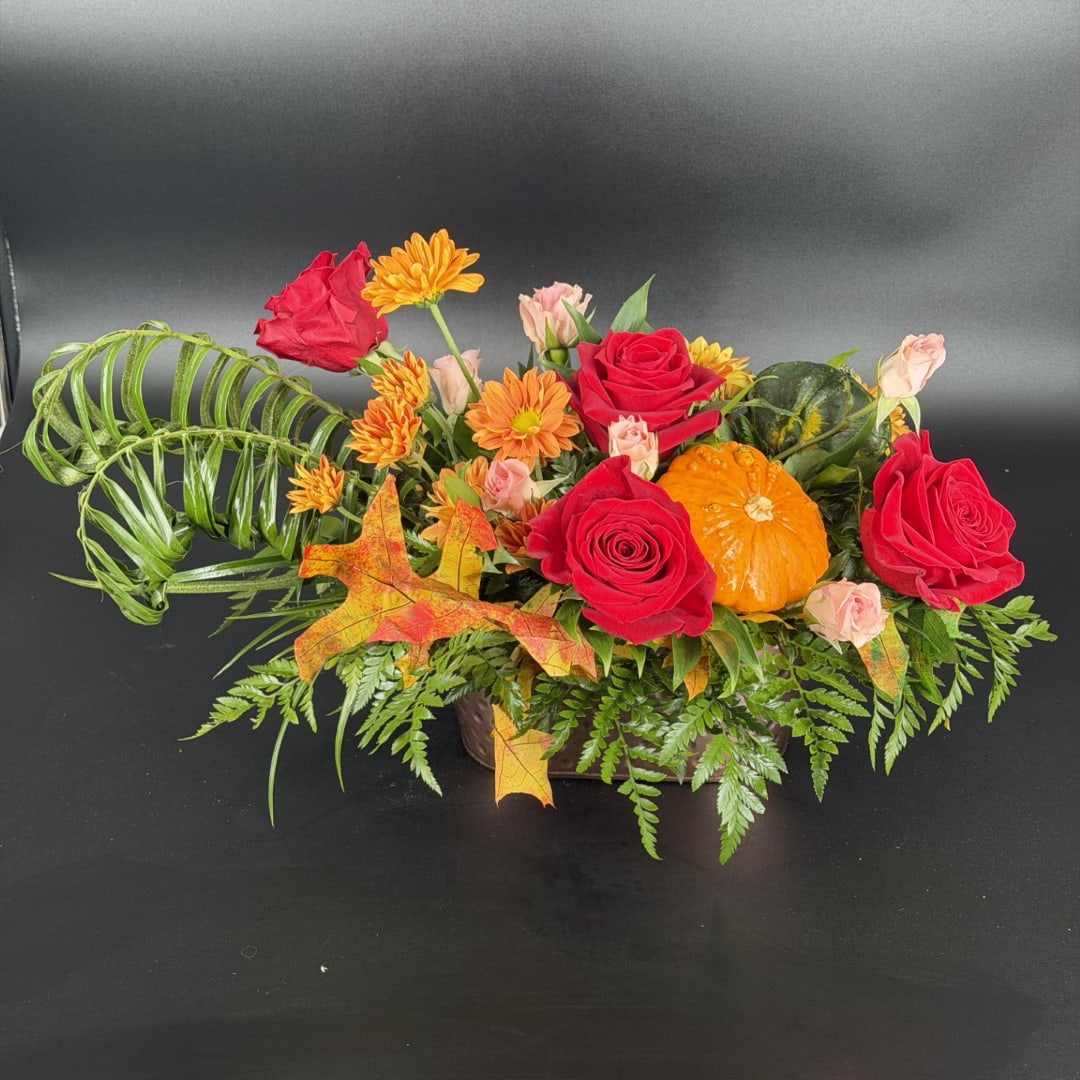 Autumn floral arrangement with red roses, orange daisies, and a small pumpkin in a low container