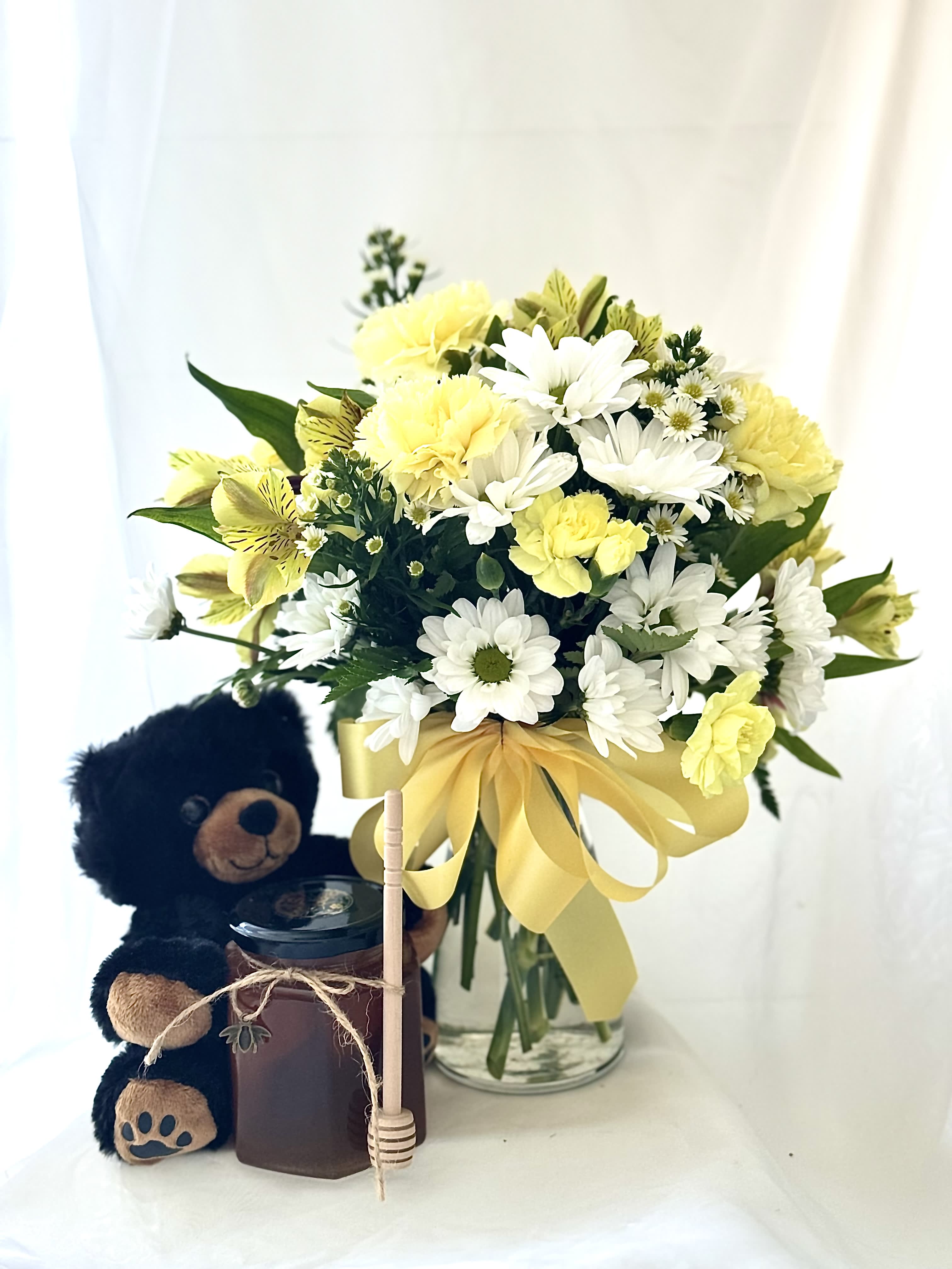Yellow and white bouquet in a glass vase with a teddy bear and candle