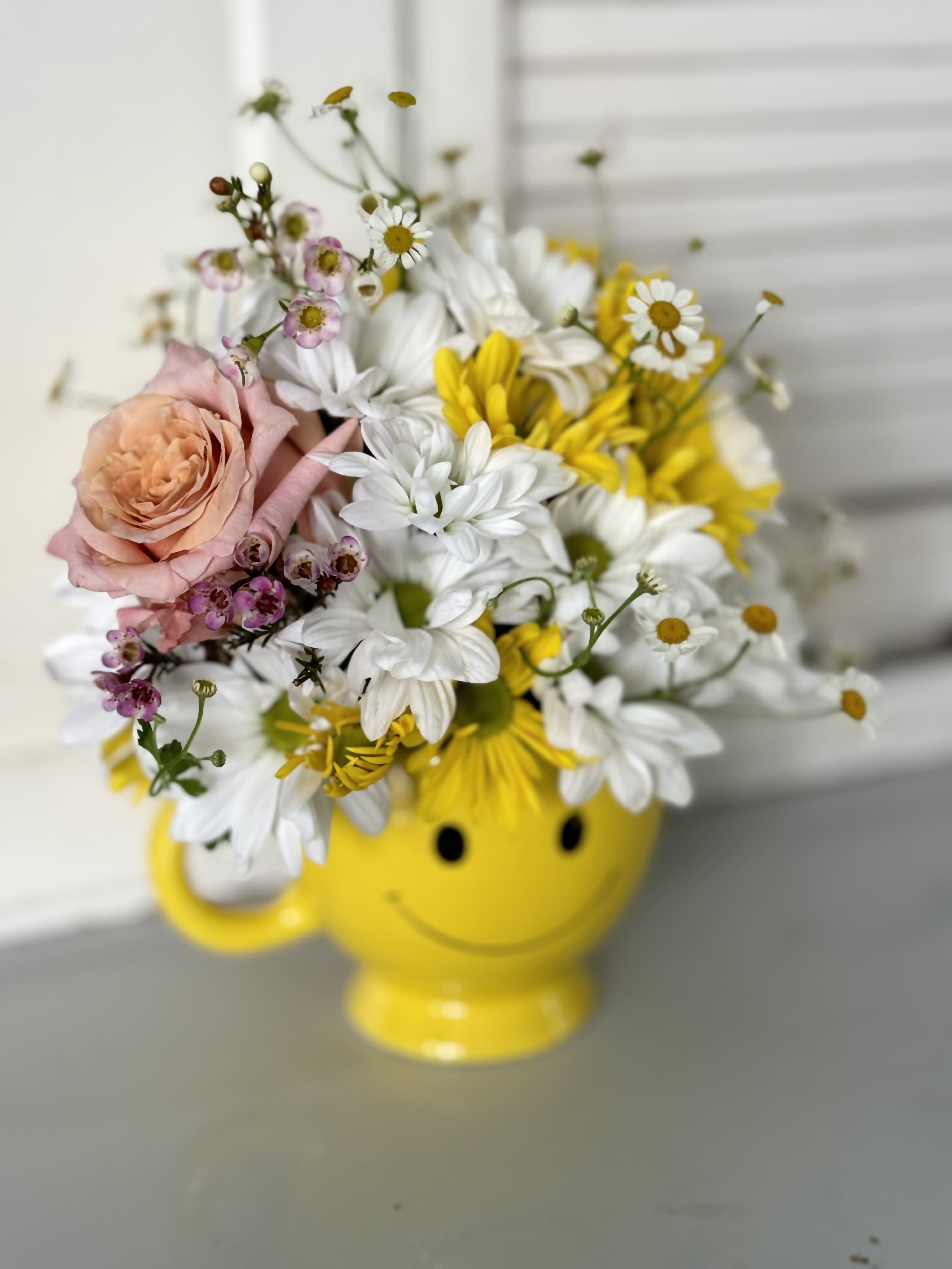 Bouquet of daisies and a peach rose in a yellow smiley-face mug