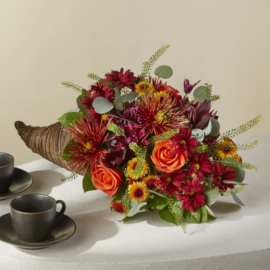 Celebrate Autumn Cornucopia - Celebrate everything you're thankful for with this iconic symbol of bounty and blessings resplendent with orange roses, bronze button pompons, red Leucadendron, and more.