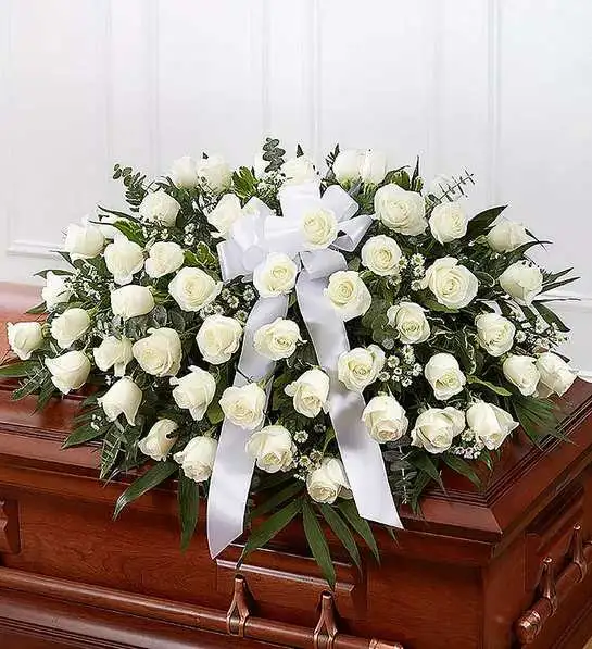 White rose casket spray with a white ribbon on a wooden casket
