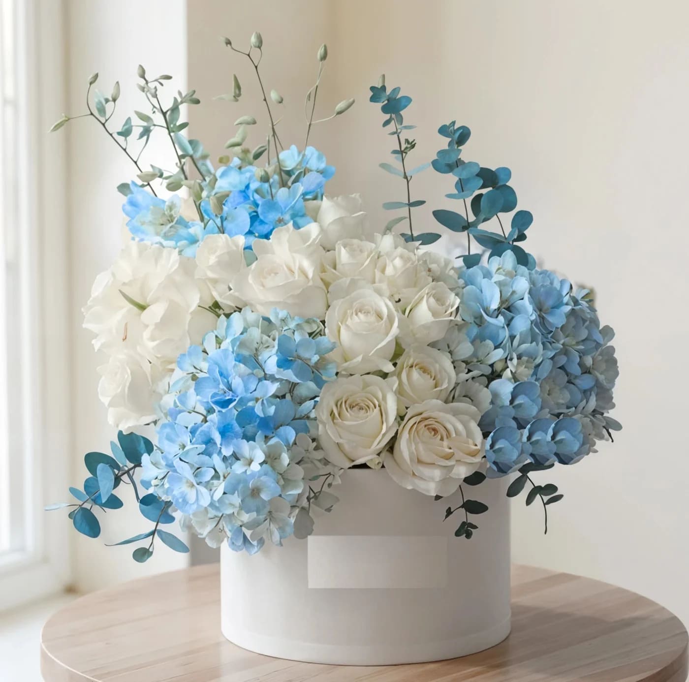 White and blue floral arrangement in a round white box