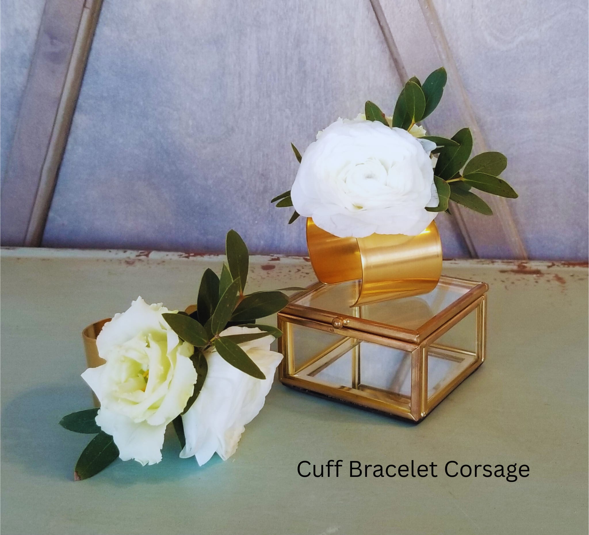 Two white floral cuff corsages with gold bracelet bands and greenery