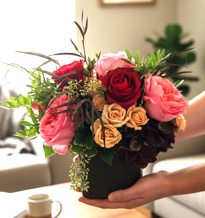 Handheld bouquet of pink and red roses in a black vase