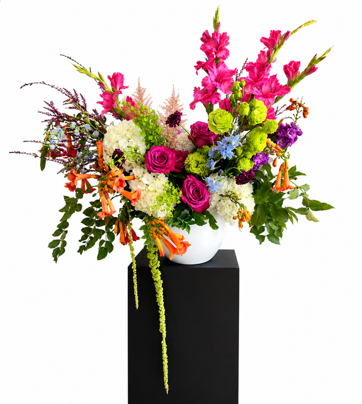 Bright mixed flower arrangement in a white vase on a black pedestal
