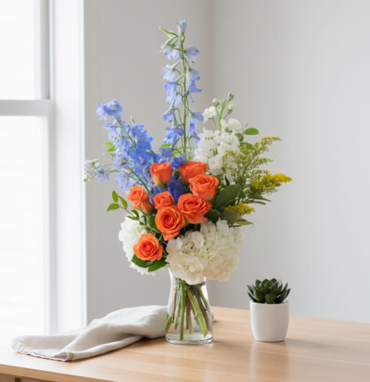 Bouquet of orange roses, blue delphinium, and white hydrangeas in a glass vase