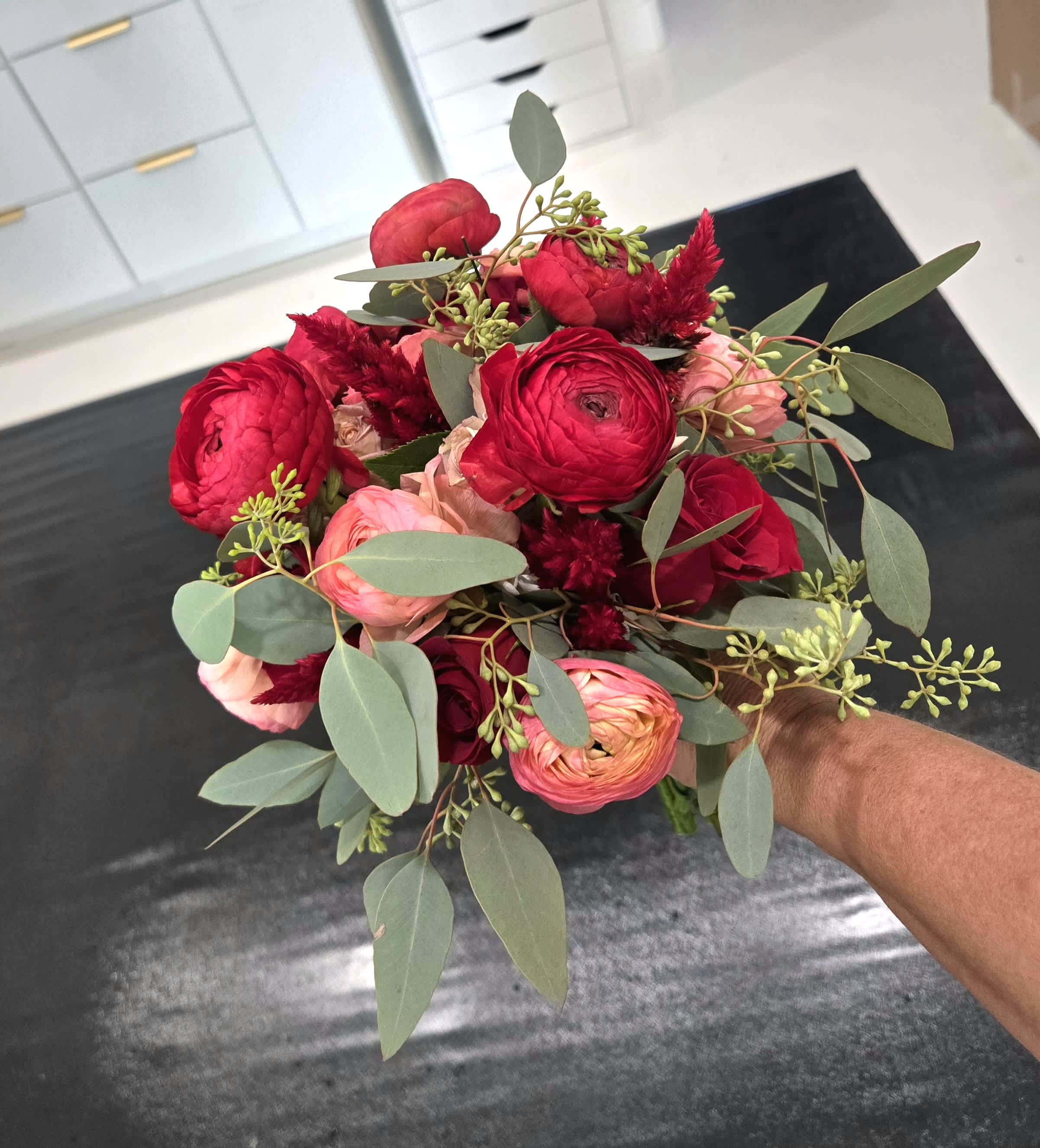Handheld bouquet of red and pink flowers with eucalyptus foliage