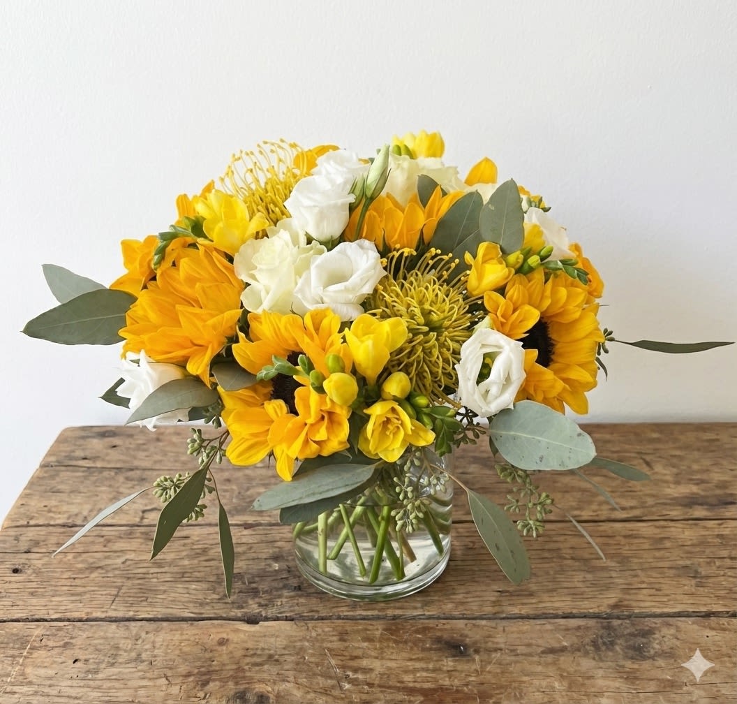 Golden Splash   - A yellow and white floral arrangement in a vase, designed to add a splash of color to your home. The combination of classic yellow sunflowers and yellow or orange tropical pincushion proteas is unique and fun. Accented with other white and yellow flowers, as well as greenery. Standard size pictured. Larger sizes available. Flowers and vase will vary based on availability.