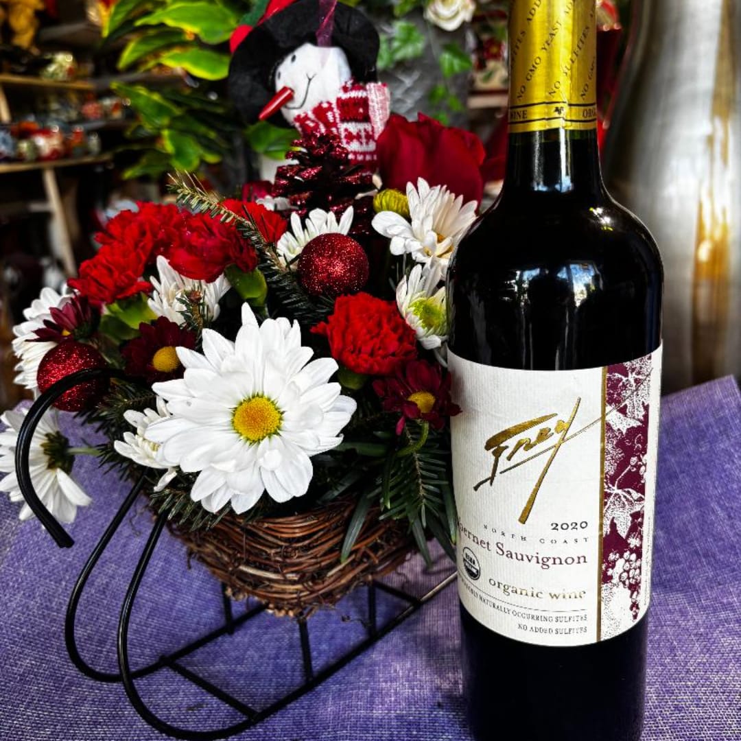 Basket arrangement with red and white flowers beside a wine bottle