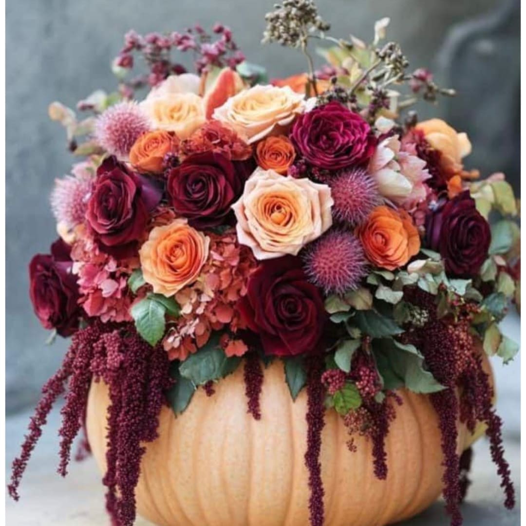 Floral arrangement in a pumpkin container with roses and trailing blooms