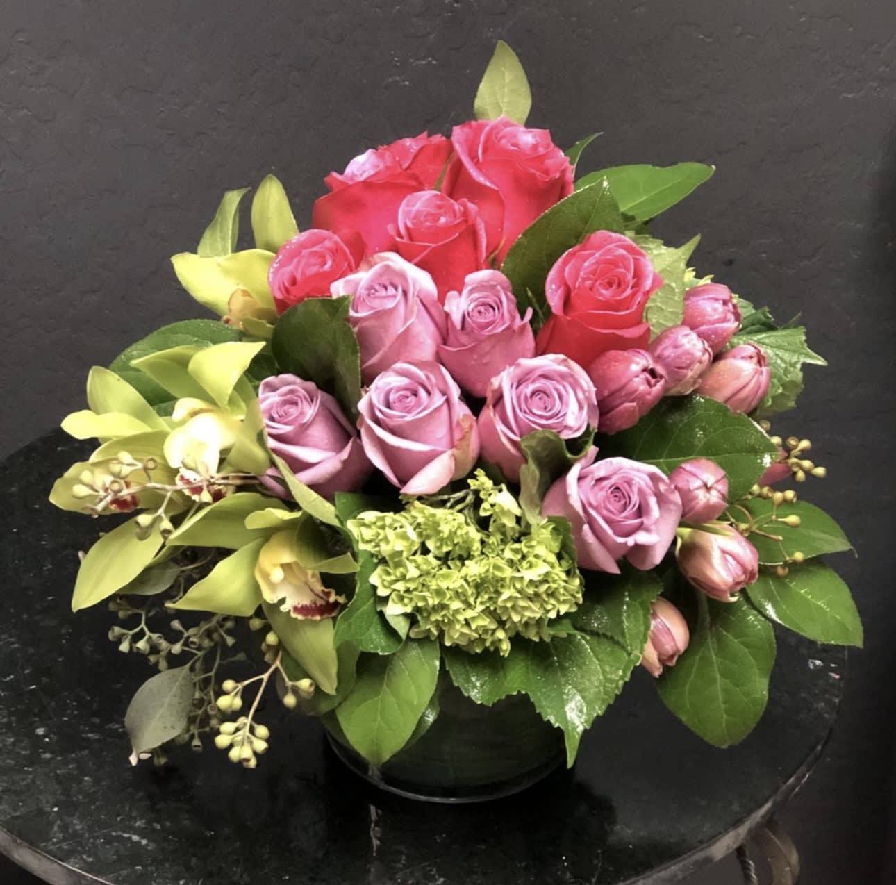 Pink and red rose bouquet with green hydrangea in a black vase