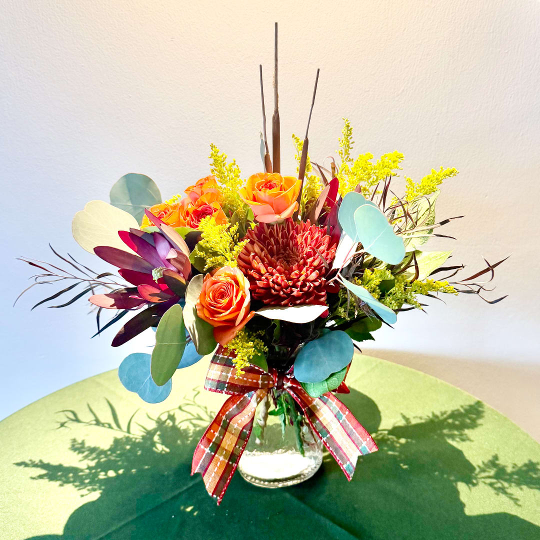 Orange roses and a red chrysanthemum in a glass vase with a plaid ribbon
