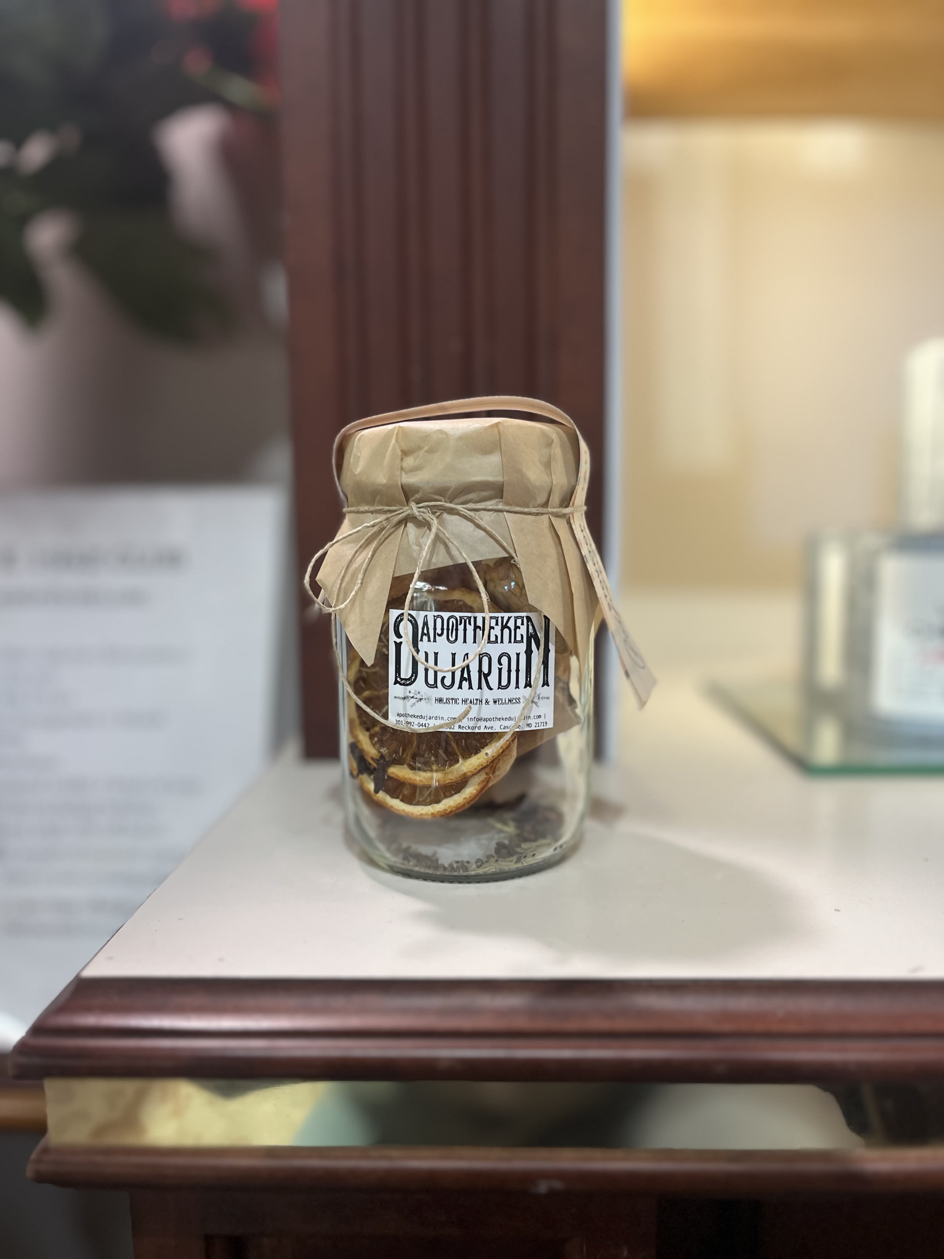 Glass apothecary jar with dried orange slices and a paper-wrapped lid on a wooden shelf.