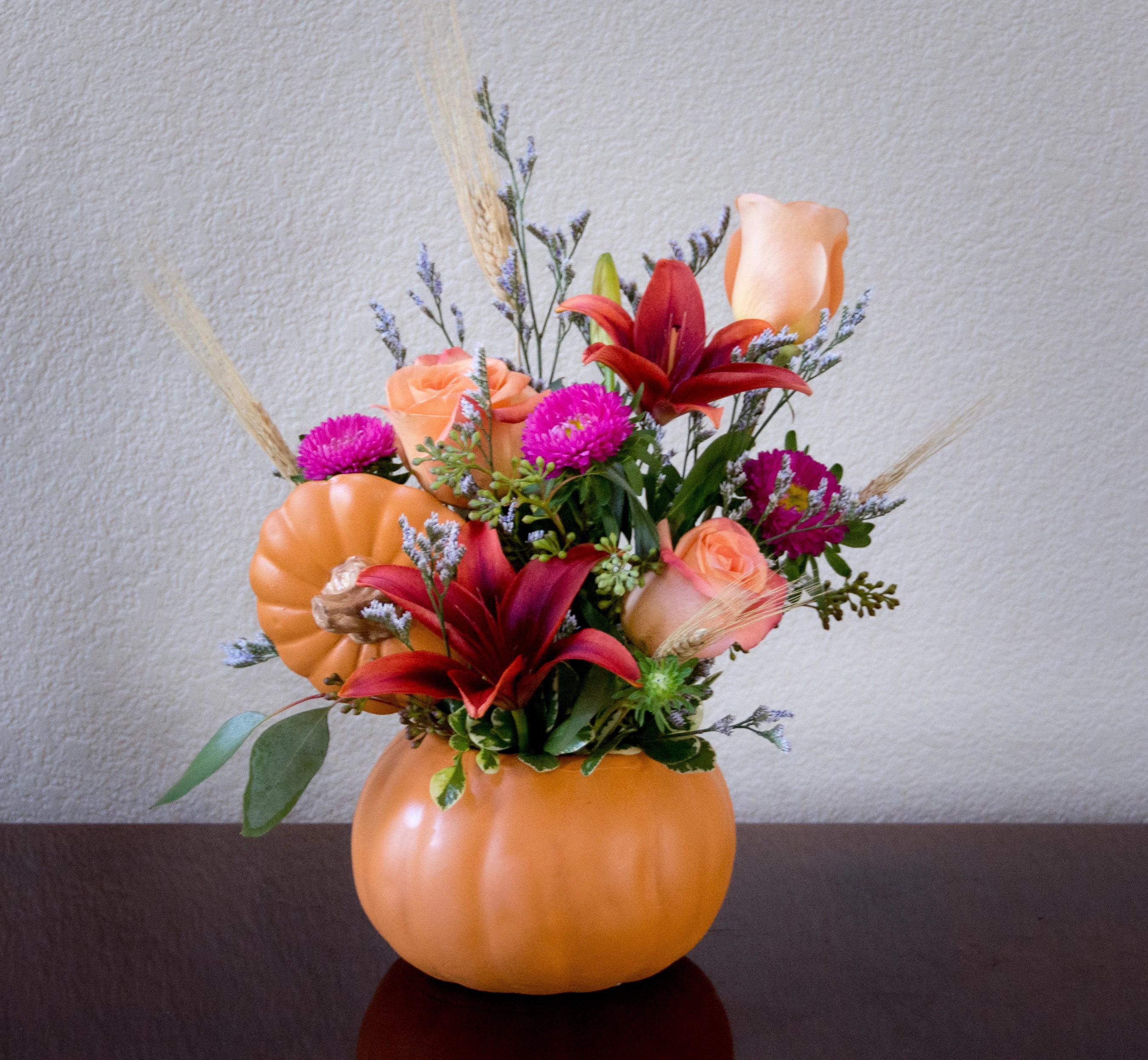 Floral arrangement in a pumpkin-shaped container with orange roses and red lilies