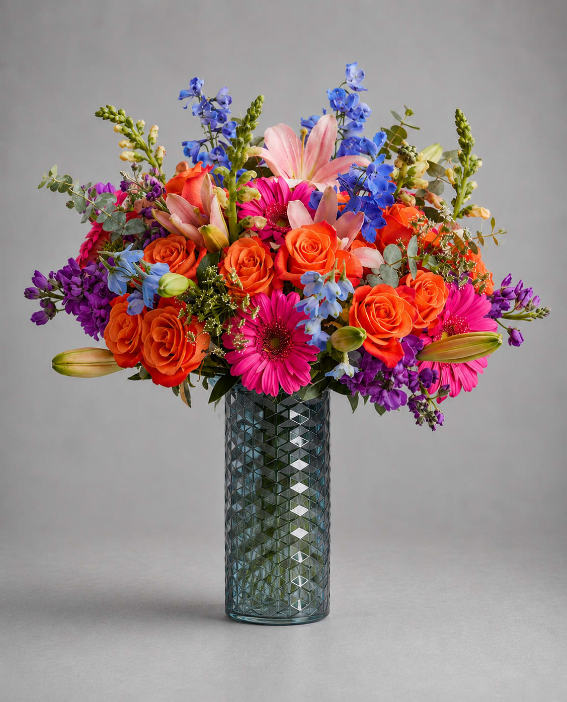 Bright mixed bouquet in a textured glass vase with roses, lilies, and daisies