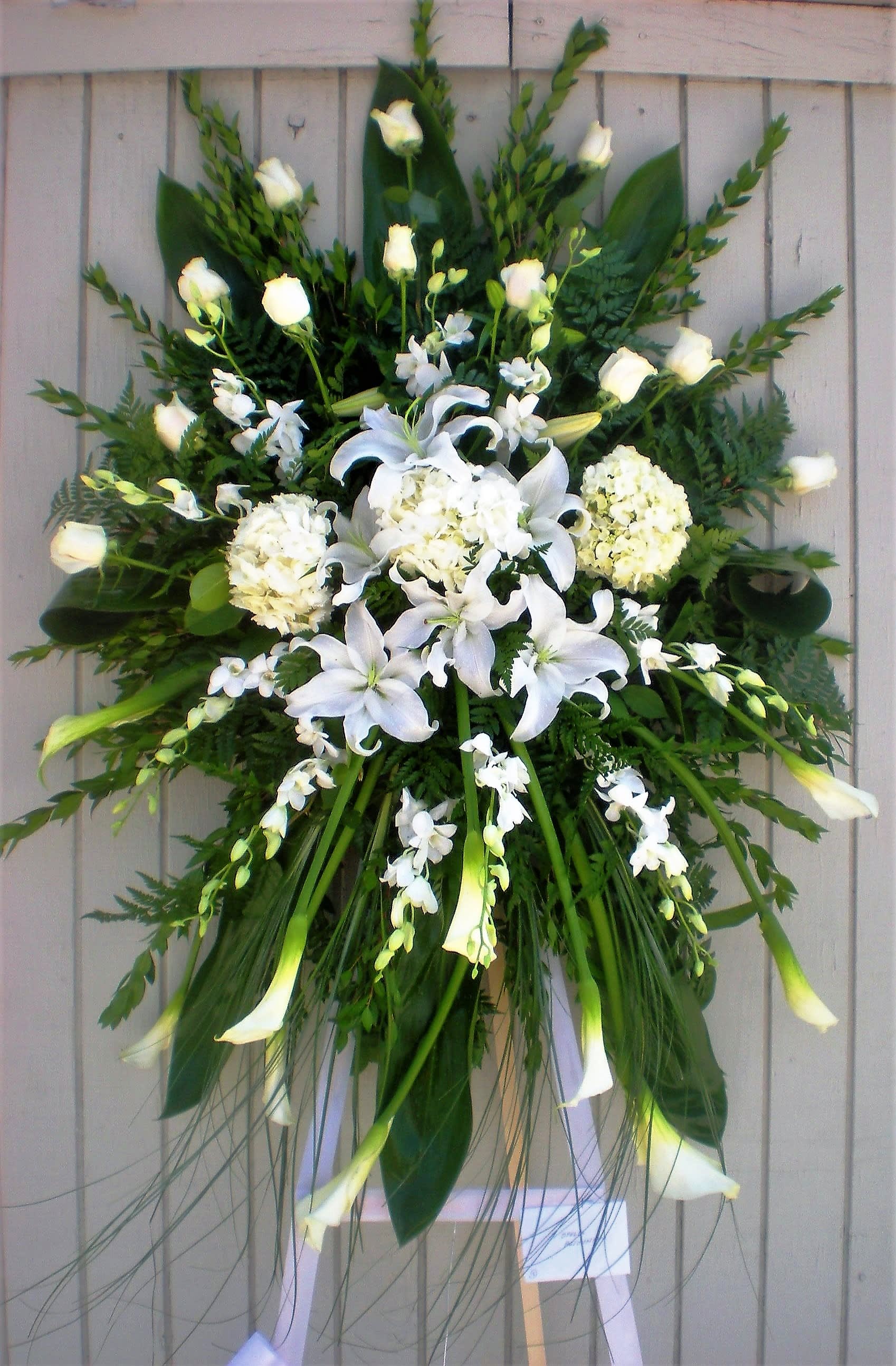 White floral standing spray with lilies, roses, and orchids