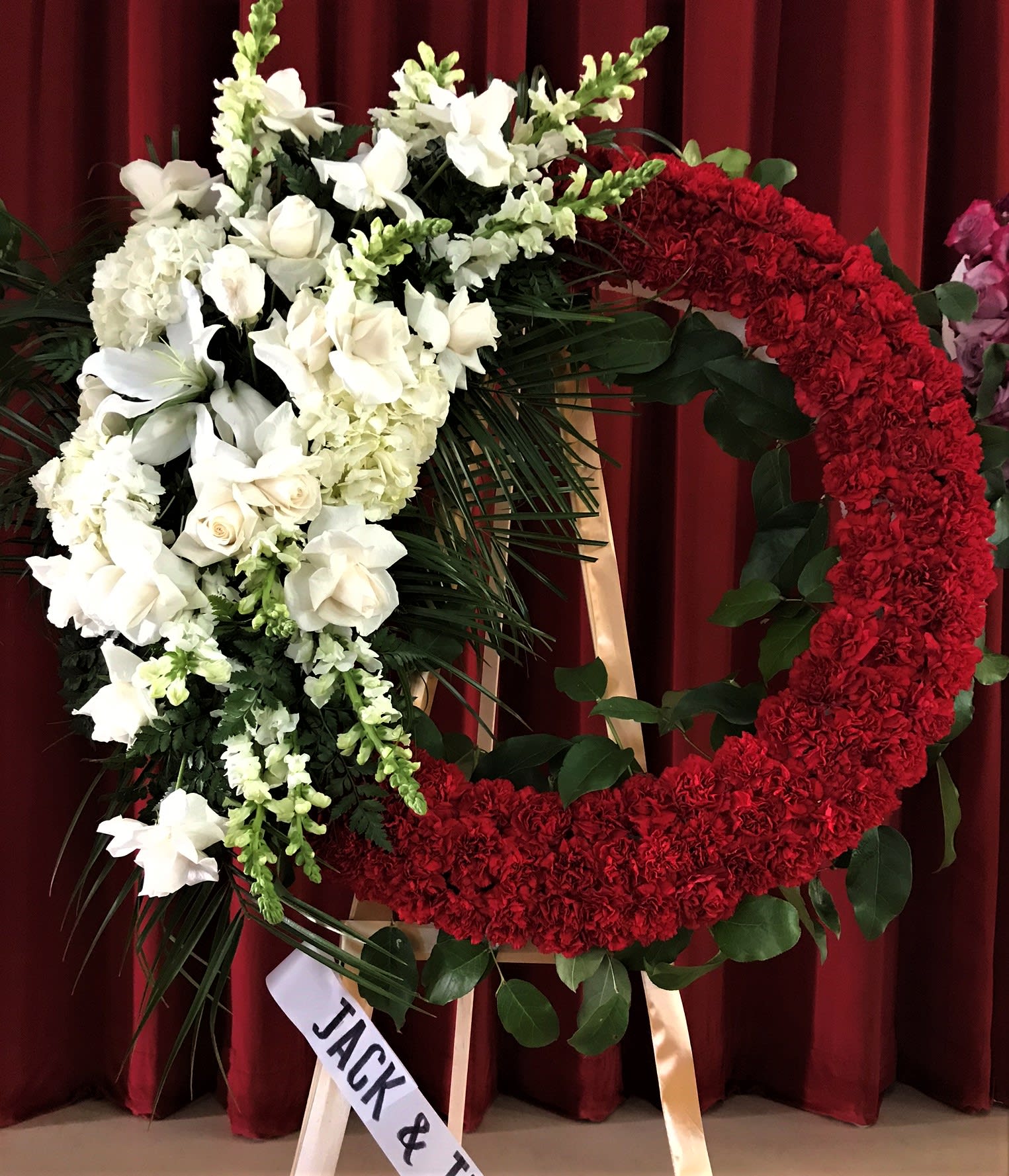 Large red and white floral wreath on a stand with a ribbon