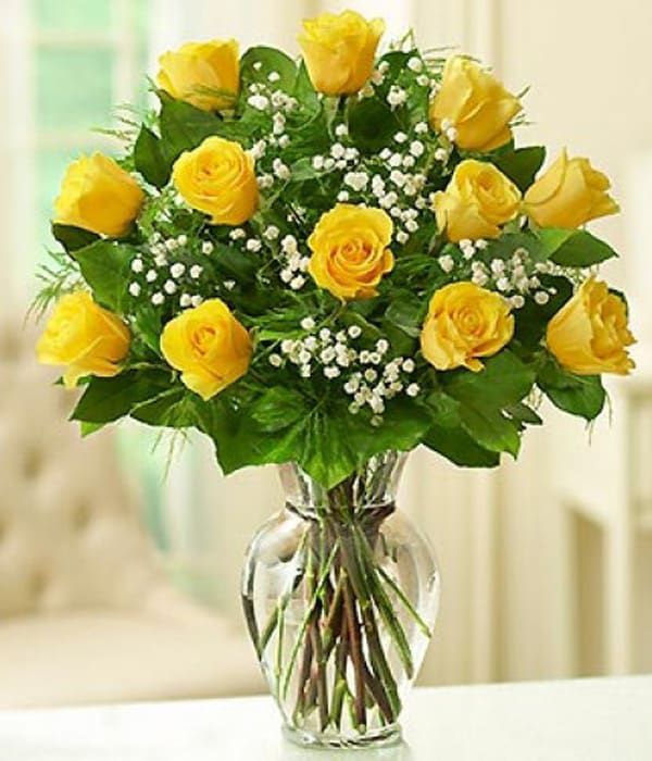 Yellow roses in a clear glass vase with white filler flowers