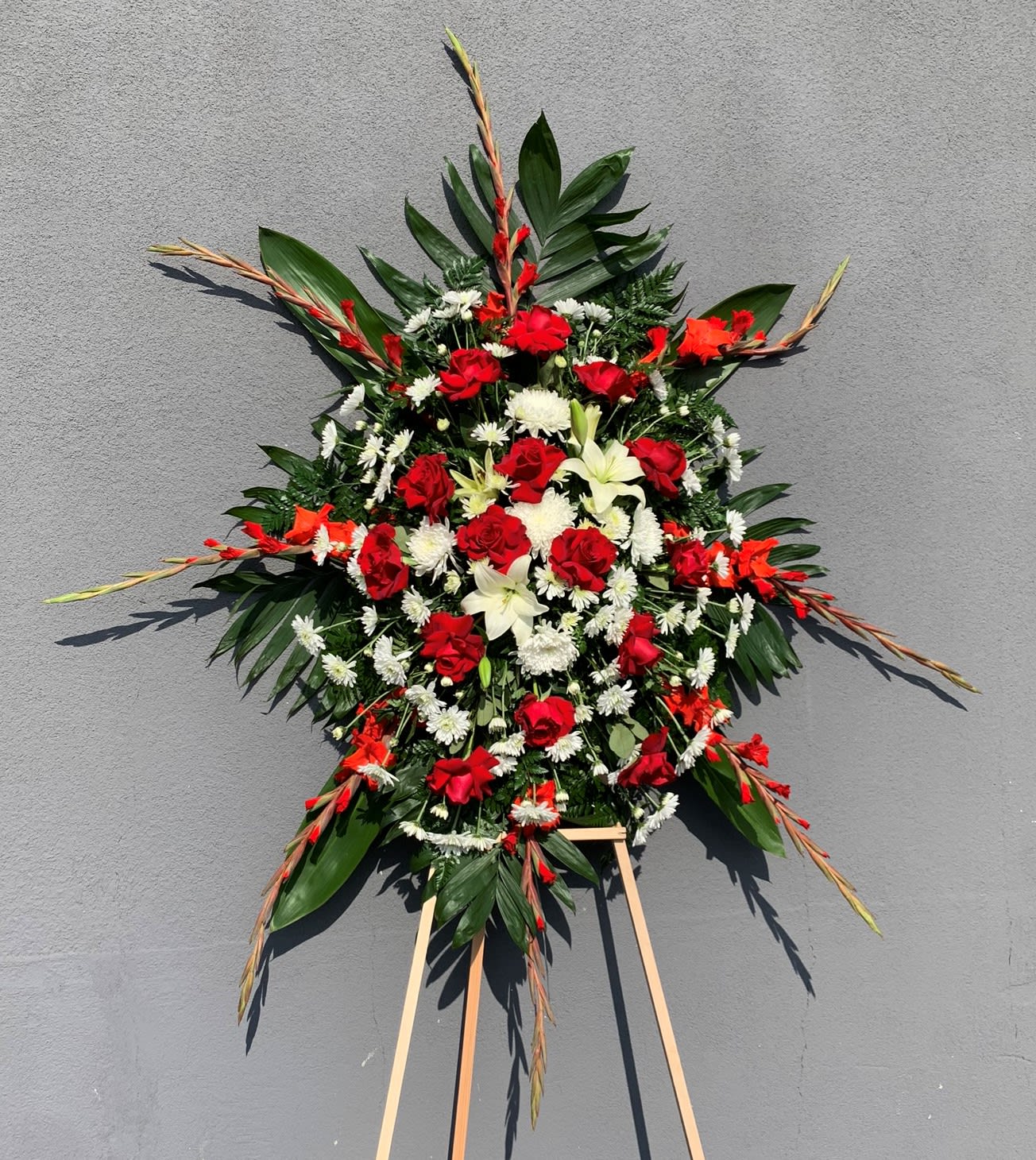 Standing floral spray with red roses, white lilies, and daisies on an easel