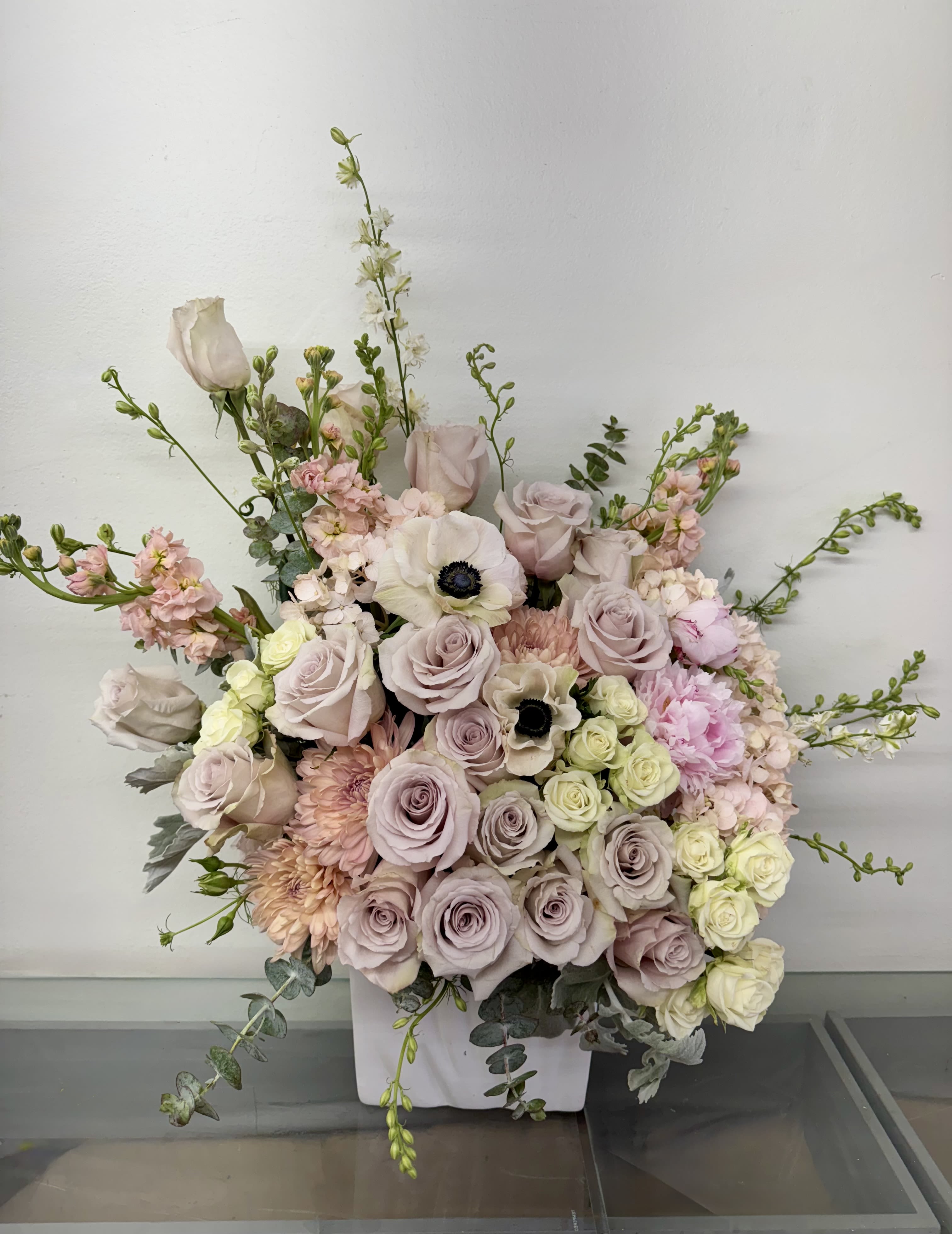 Large pastel floral arrangement in a white vase with roses and anemones