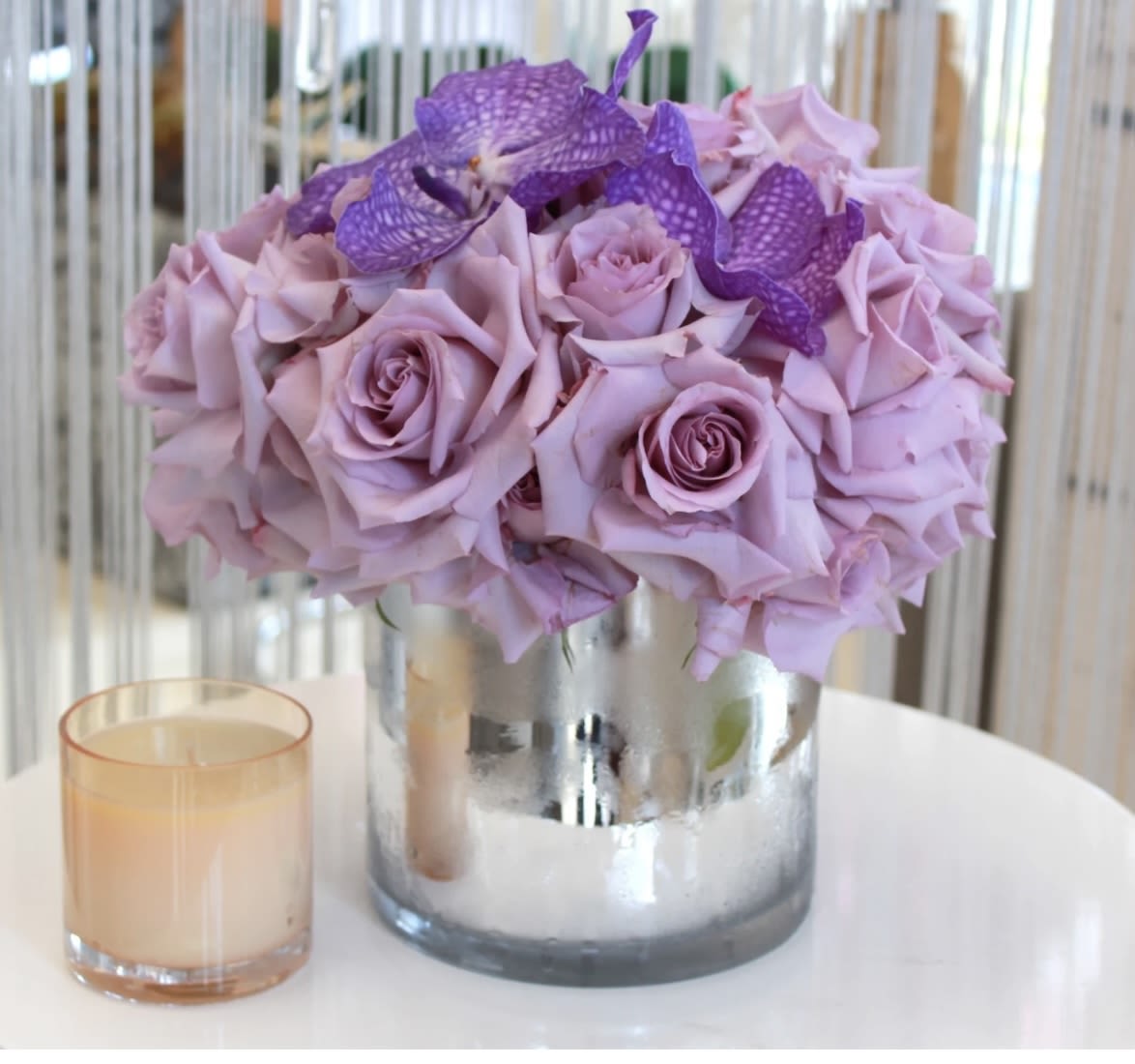 Lavender rose bouquet in a silver vase with a small candle beside it