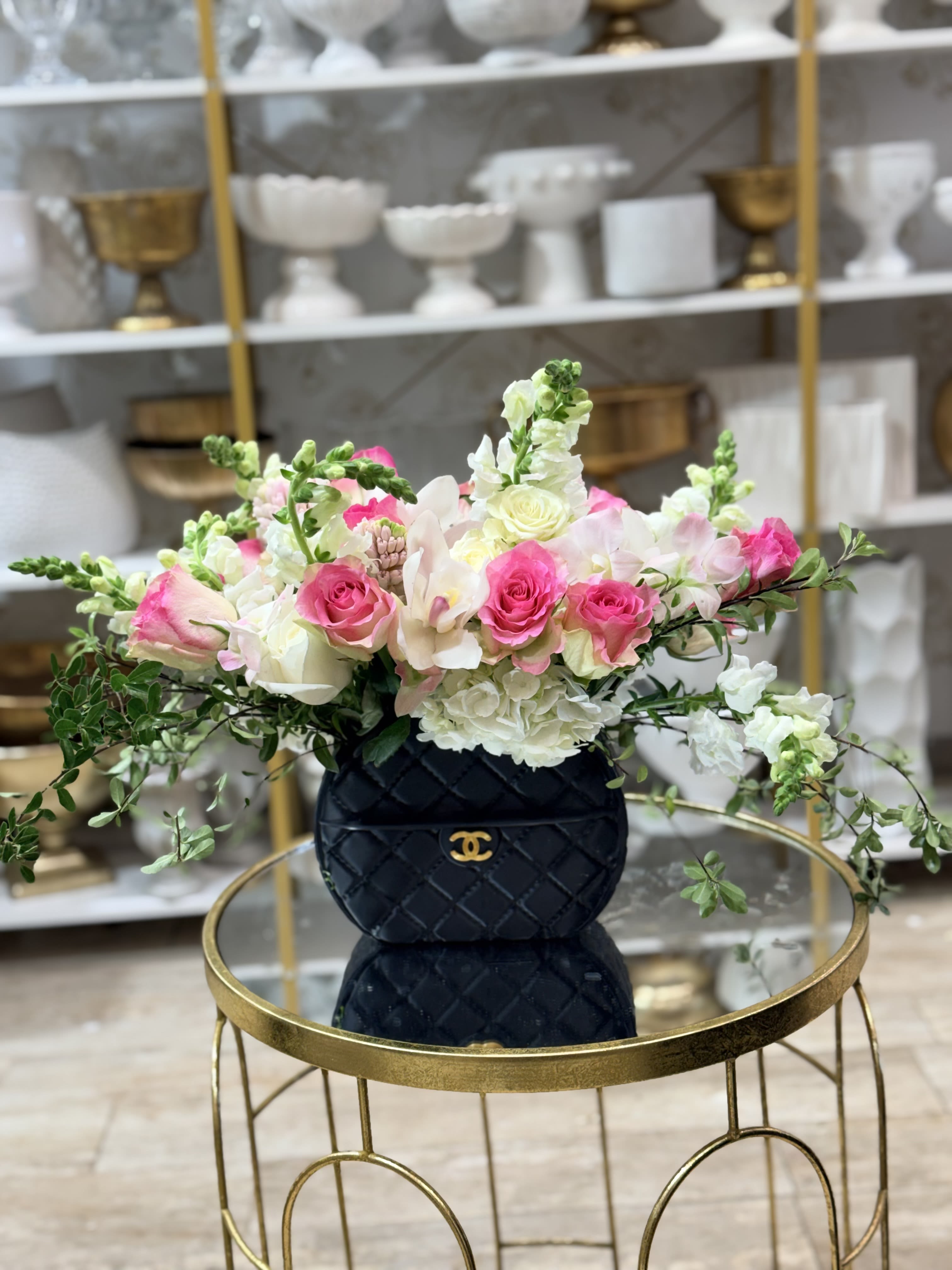 Sassy Girl  - Bright pink and white roses mingle with pale lisianthus, white hydrangea and tall snapdragon spikes in a compact, full arrangement designed to make her feel noticed. This flower arrangement for Mother's Day, anniversaries or birthdays pairs romantic blooms with a bold black Designer quilted vase, so it reads equally as a love-and-romance gift or a polished centerpiece for a wedding-adjacent celebration.  The palette-vivid pinks, crisp whites and fresh green foliage-creates a feminine, modern contrast against the structured black vase with a gold emblem. Hydrangeas add lush volume, roses bring classic romance, lisianthus lends soft, ruffled texture and the snapdragons add vertical drama. The flowers spill outward from the vase for a generous, garden-picked look.  Perfect for saying "thinking of you," "thank you," "get well" or "congrats on the new baby," this arrangement suits anyone you want to make feel truly seen. Sized as a compact yet full display, it arrives ready to display-simply add water and enjoy the layered textures and long-lasting blooms.