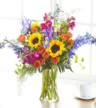 Colorful bouquet with sunflowers, roses, and blue flowers in a glass vase