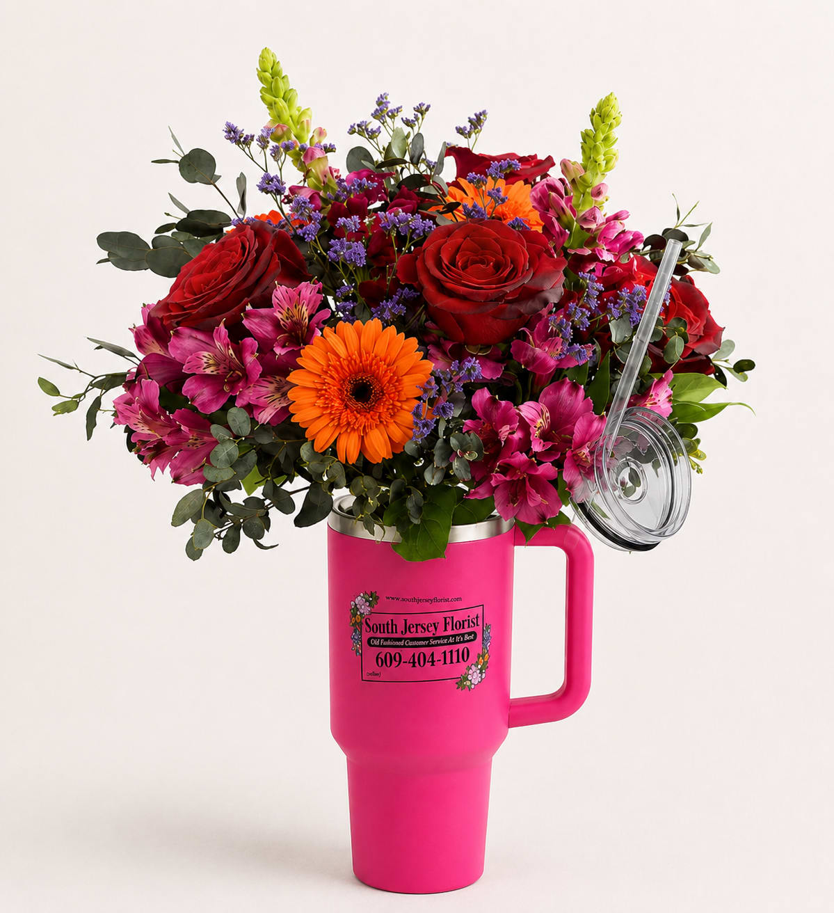 Mixed bouquet of red roses, orange gerbera daisies, and pink flowers in a pink tumbler vase