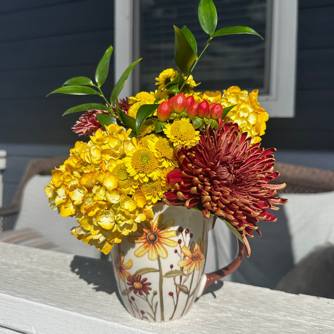 Yellow and red chrysanthemum arrangement in a floral mug vase