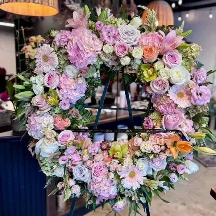 Standing Floral Wreath – Funeral &amp; Sympathy Flower Arrangement - Honor the memory of a loved one with our Standing Floral Wreath, a beautiful and thoughtful funeral flower arrangement. Expertly handcrafted with fresh, seasonal blooms, this floral tribute provides comfort and peace during times of remembrance. Each wreath is designed in your selected color palette, using unique, elegant flowers to reflect your personal style and sentiment.  Perfect for funeral services, memorial ceremonies, graveside displays, places of worship, or post-service receptions, this arrangement is mounted on a floral foam base to ensure lasting freshness throughout the event.  Available in a variety of shapes and sizes, including classic round wreaths, crosses, hearts, letters, and squares, our customizable standing floral wreaths offer a meaningful way to say goodbye. Choose your preferred flower colors, and our skilled florists will craft a stunning, compassionate display.  (Premium size pictured.)  Product ID: 1642 