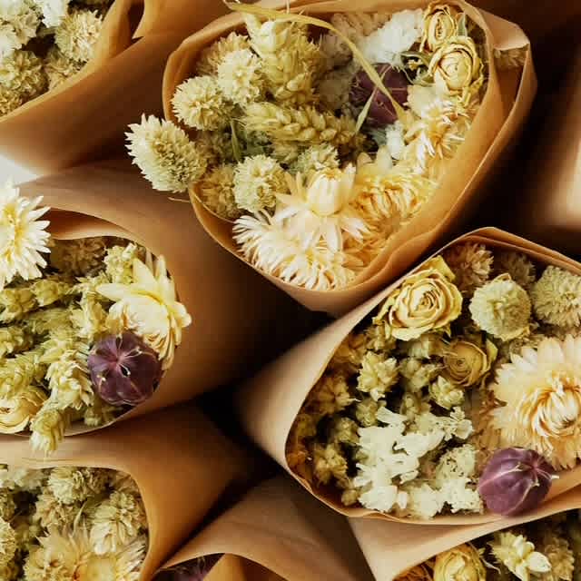 Bouquets of pale yellow and white dried flowers wrapped in brown paper