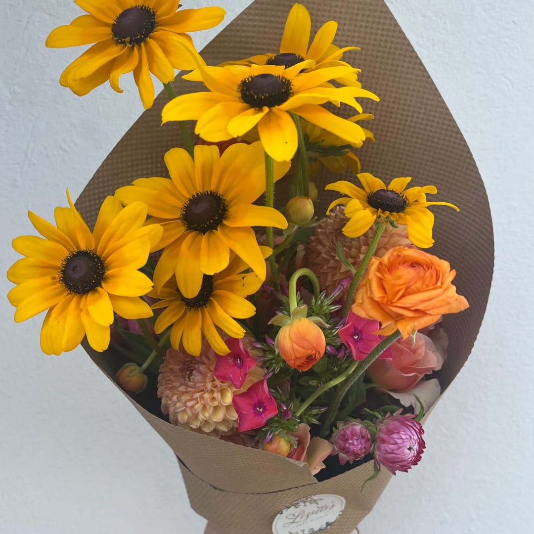 Bouquet of yellow daisies with orange and pink flowers in brown paper wrap