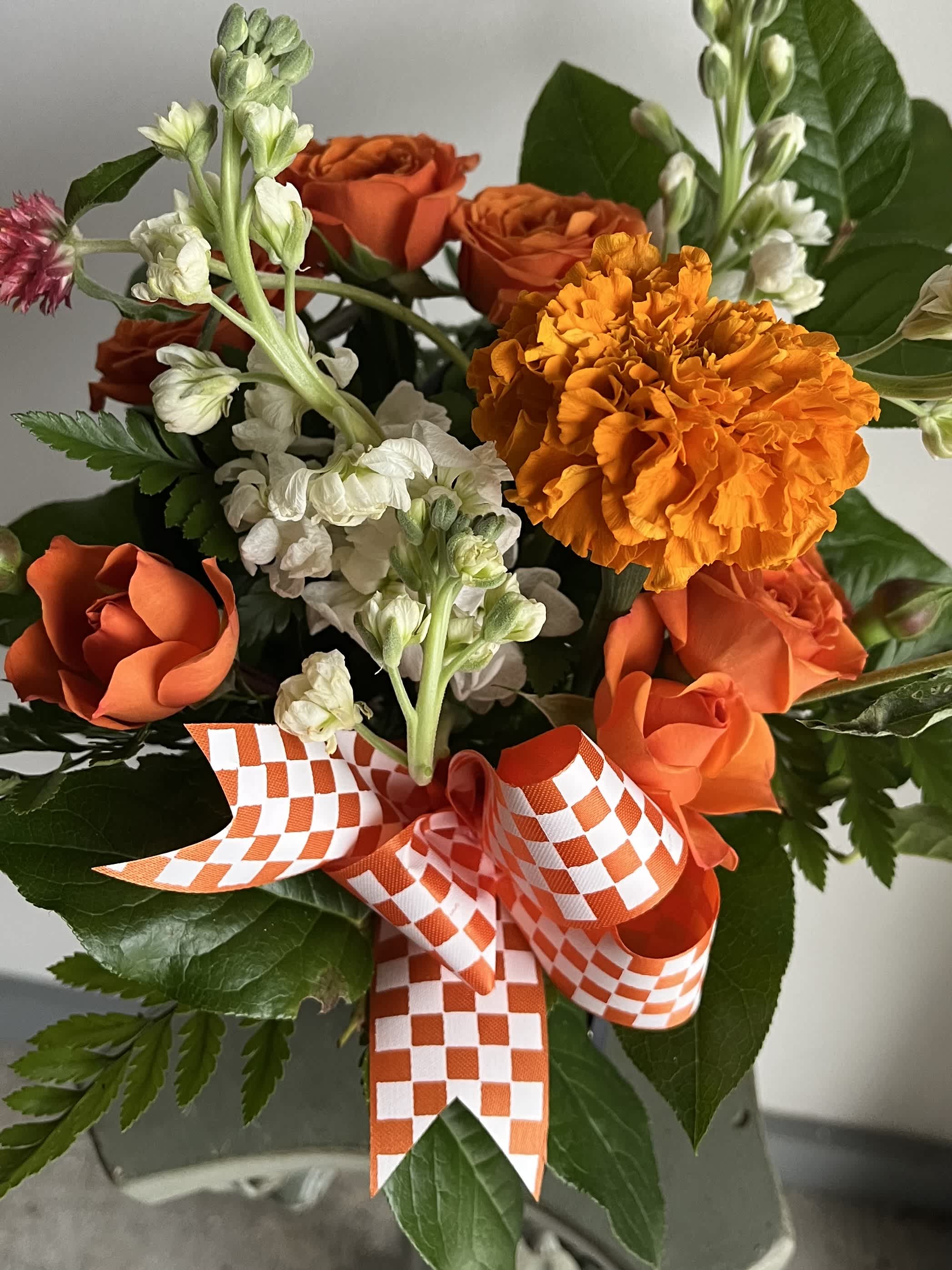 Orange roses and marigold bouquet with white flowers and checkered ribbon