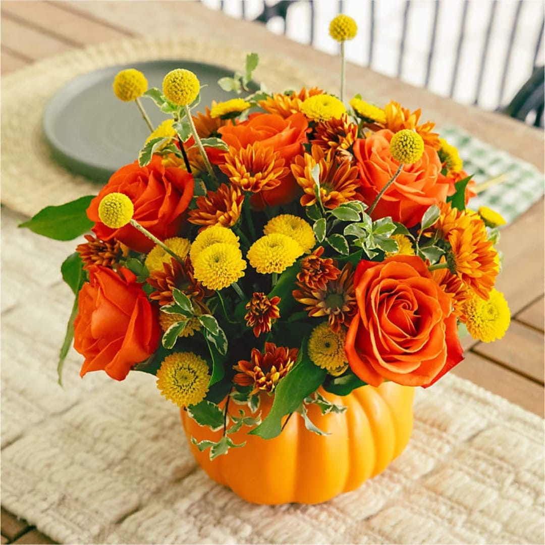 Orange roses and yellow pom flowers arranged in a pumpkin vase