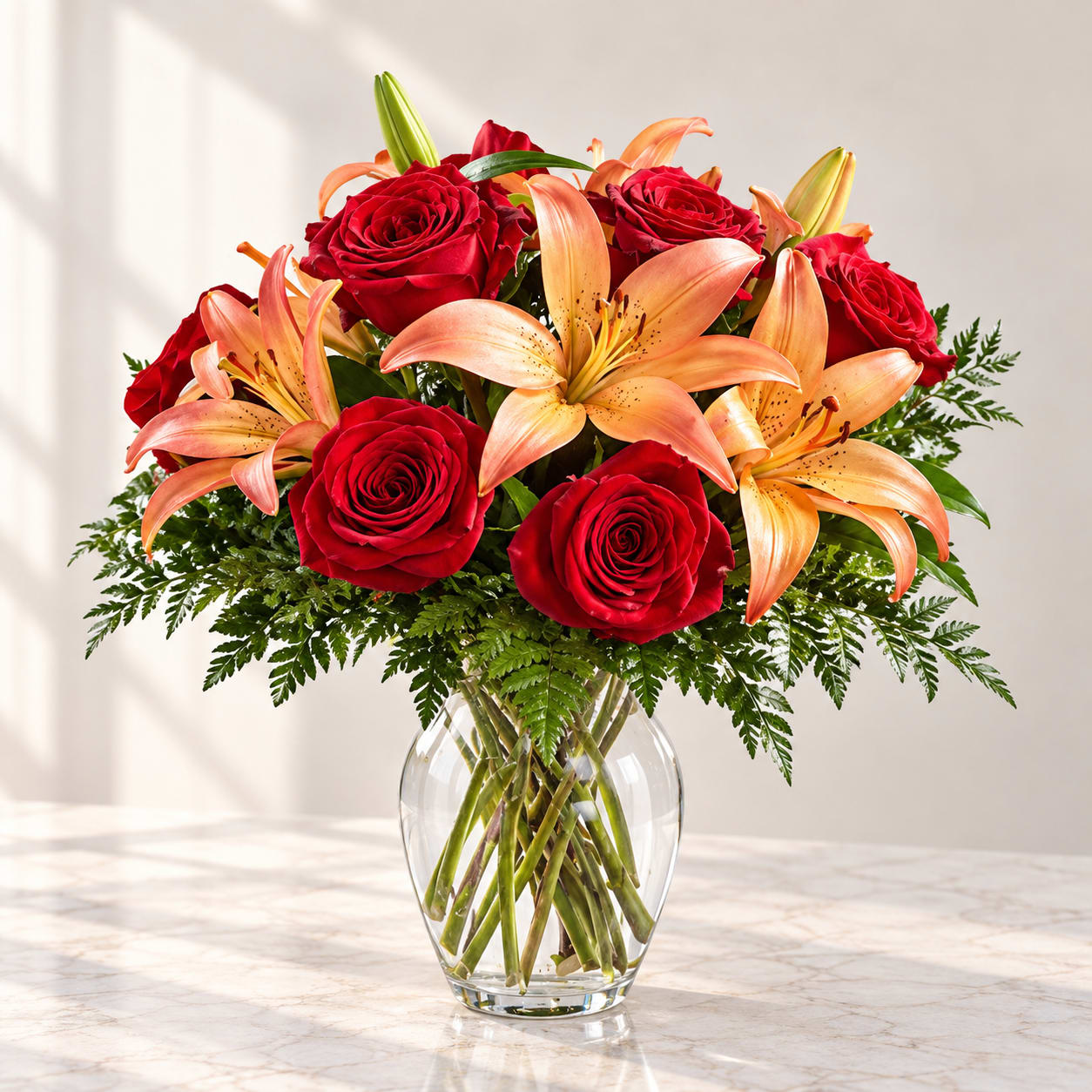 Red roses and peach lilies arranged in a clear glass vase