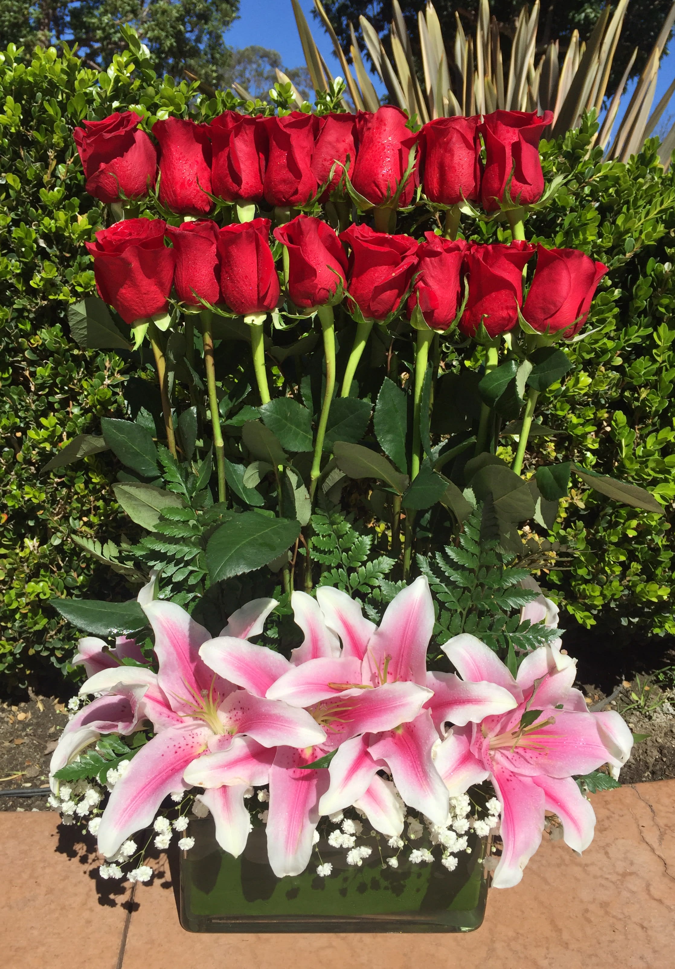 Red roses above pink-and-white lilies in a glass vase