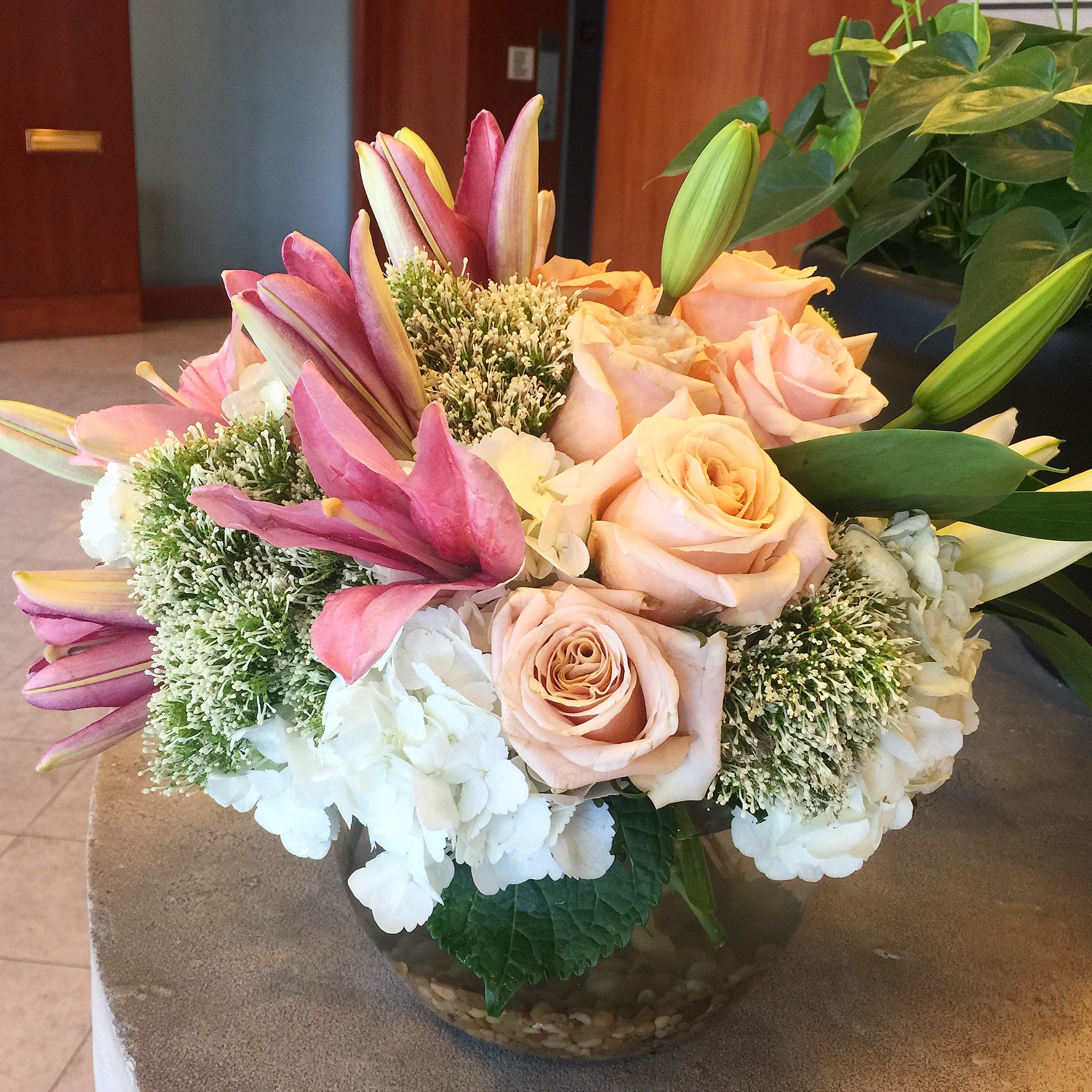 Bouquet of pink roses, lilies, and white hydrangeas in a glass bowl vase