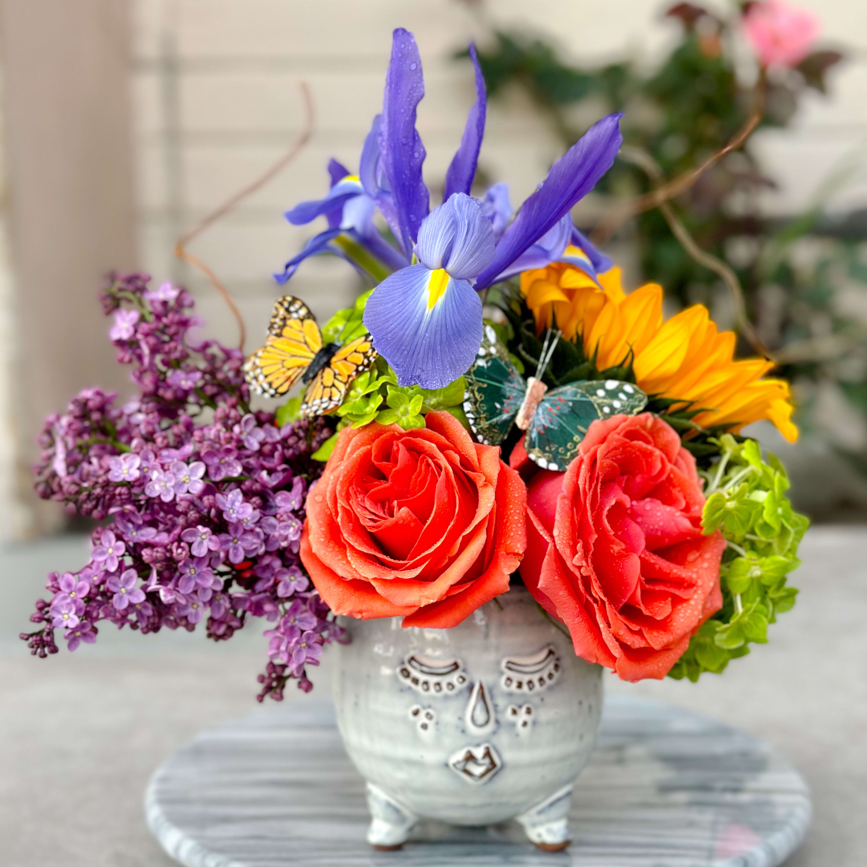 Colorful bouquet in a decorative ceramic face vase with roses and iris