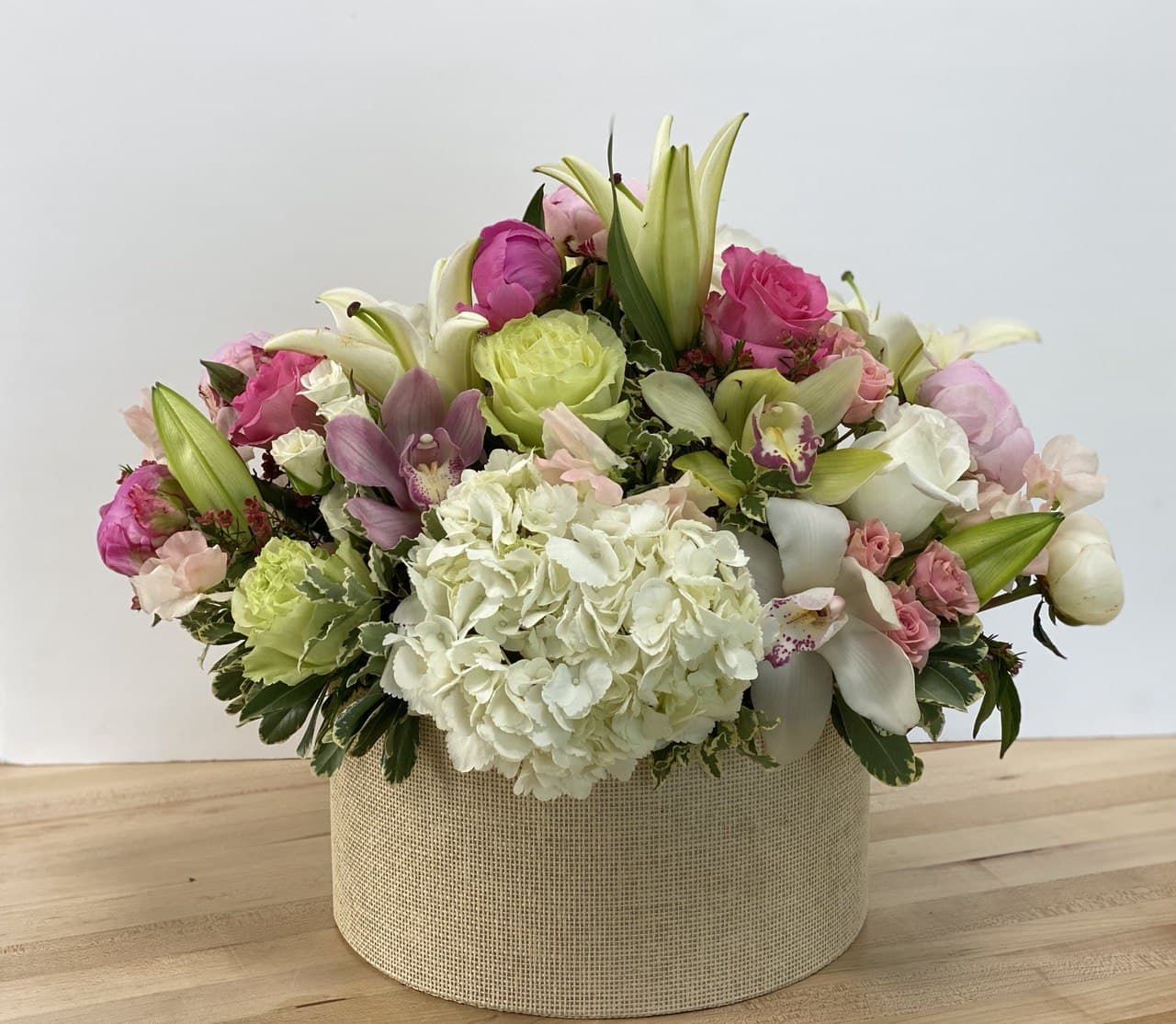 Mixed pink and white floral arrangement in a round beige box