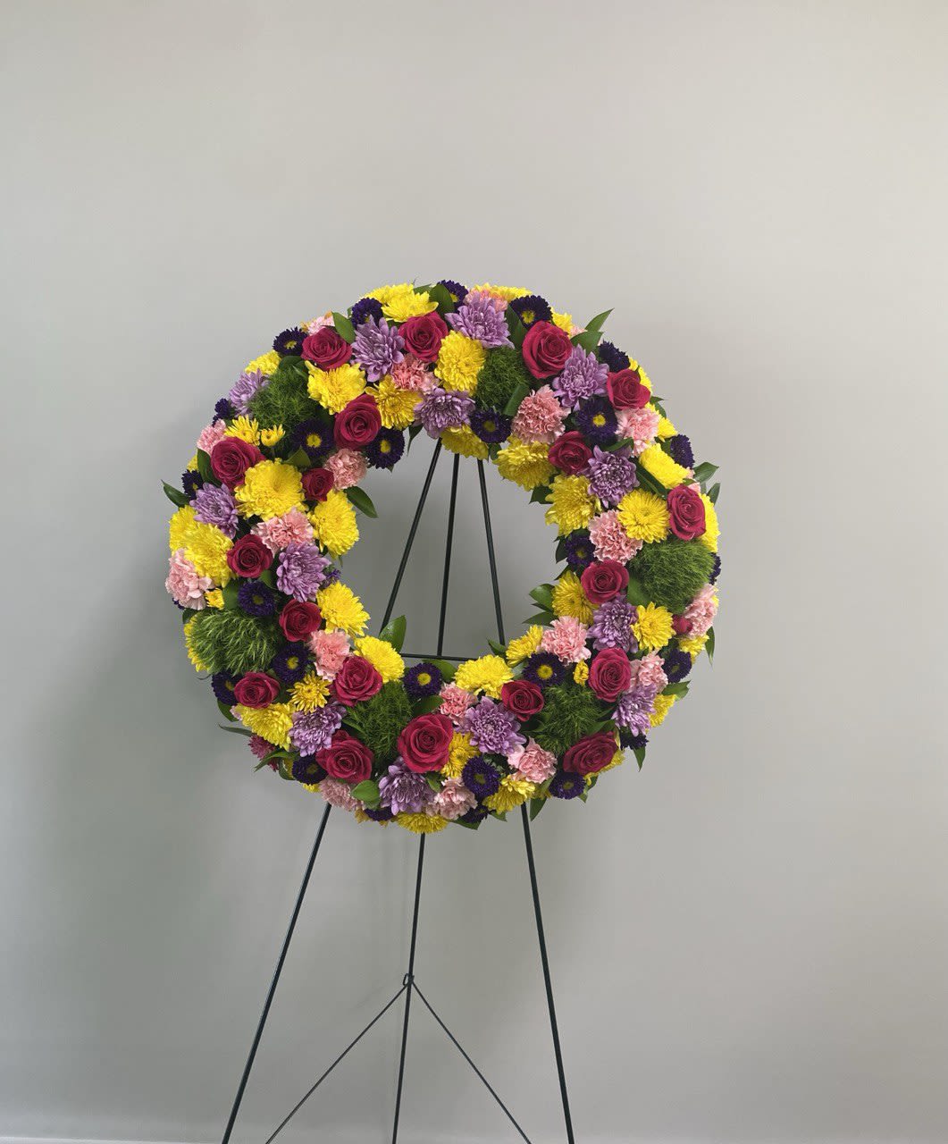 Circular floral wreath on a black stand with pink, yellow, and purple flowers