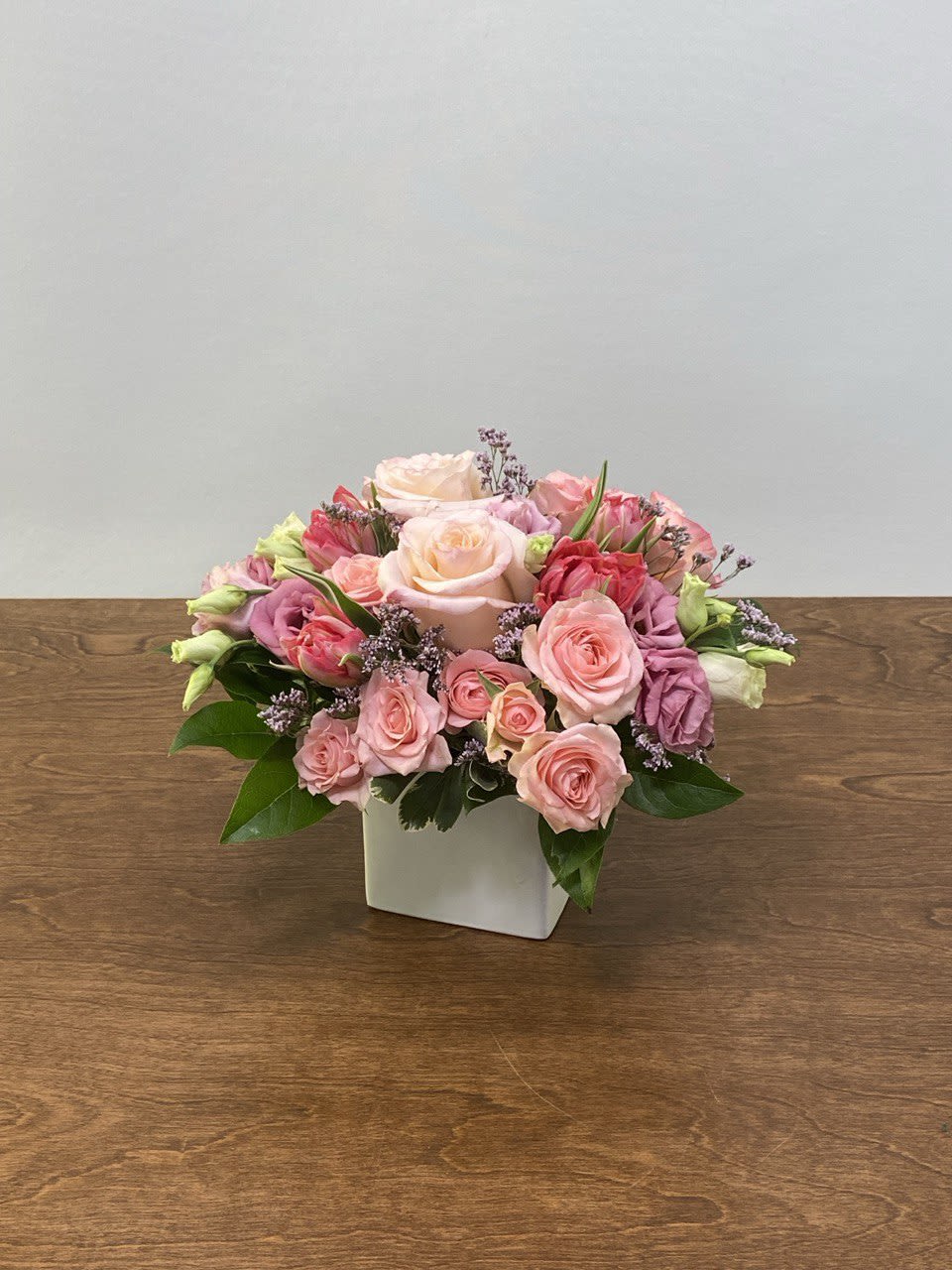 Pink and peach roses arranged in a white square vase