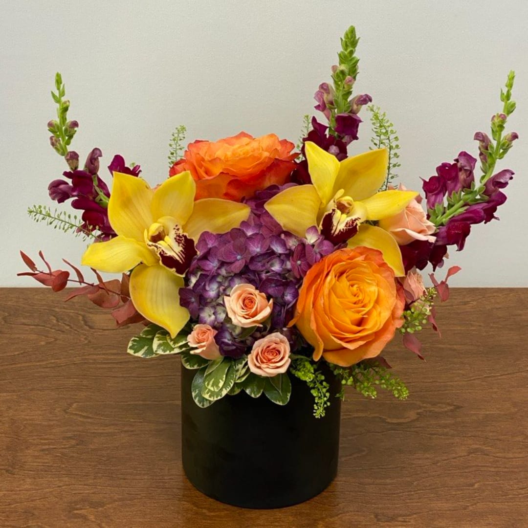 Orange roses and yellow orchids in a black vase with purple blooms
