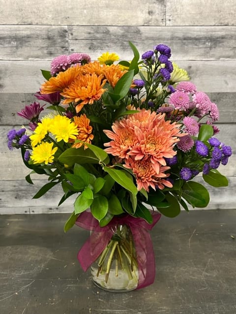Mum Madness - A delightful assortment  of chrysanthemums and asters to celebrate the fall season, with a beautiful bow to accent the arrangement.  Colors may vary.