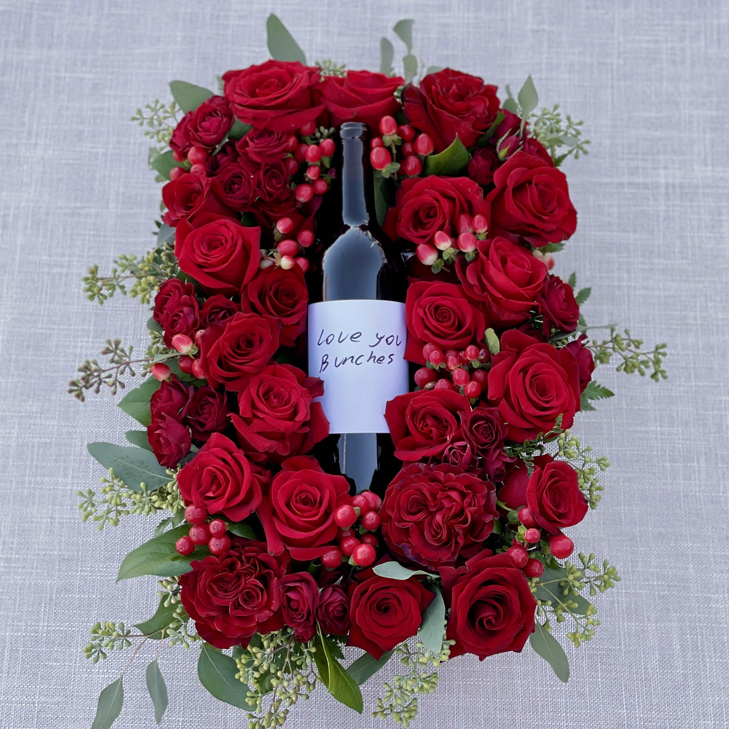 Red roses arranged around a wine bottle with a love note