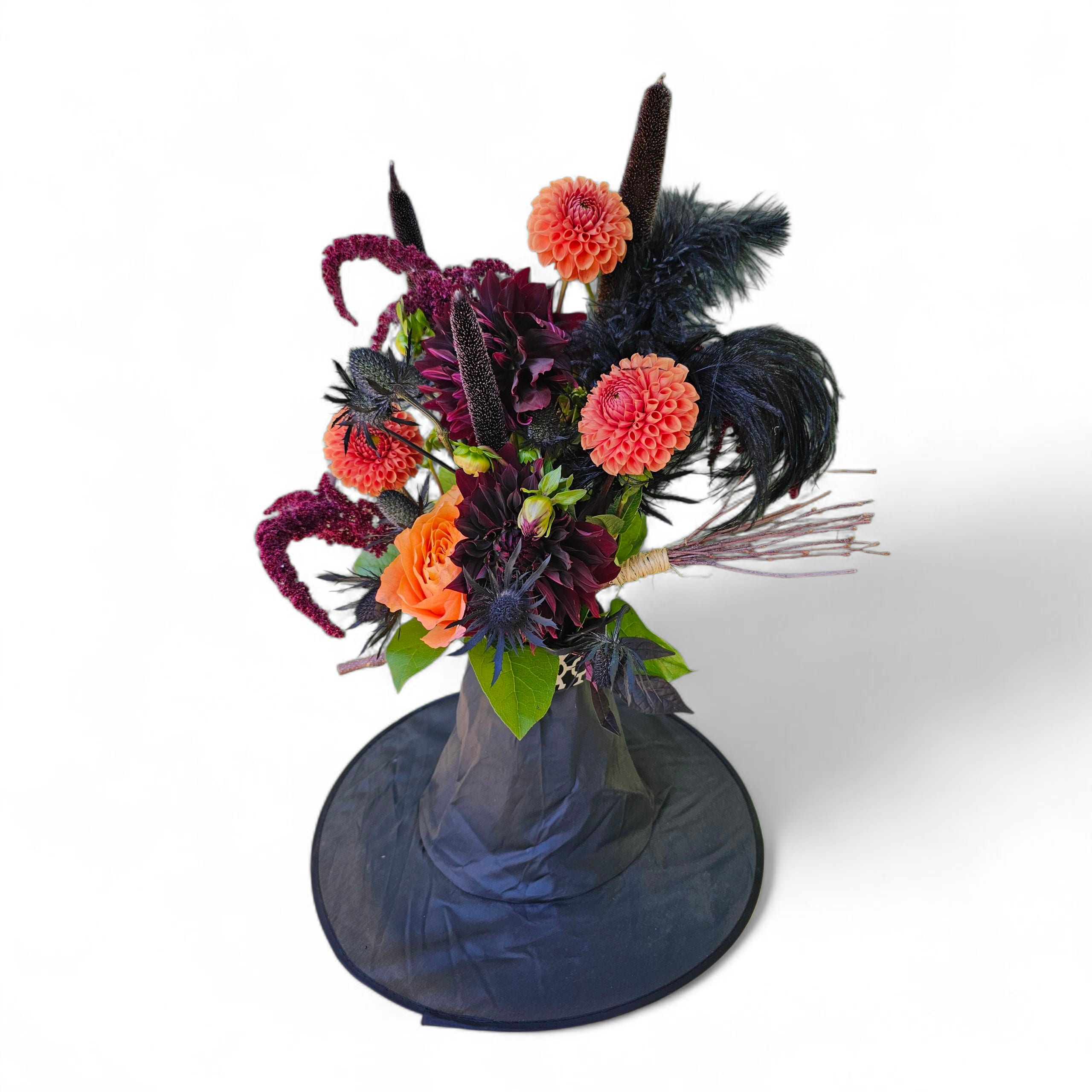 Dark floral arrangement in a black hatbox with orange and plum blooms