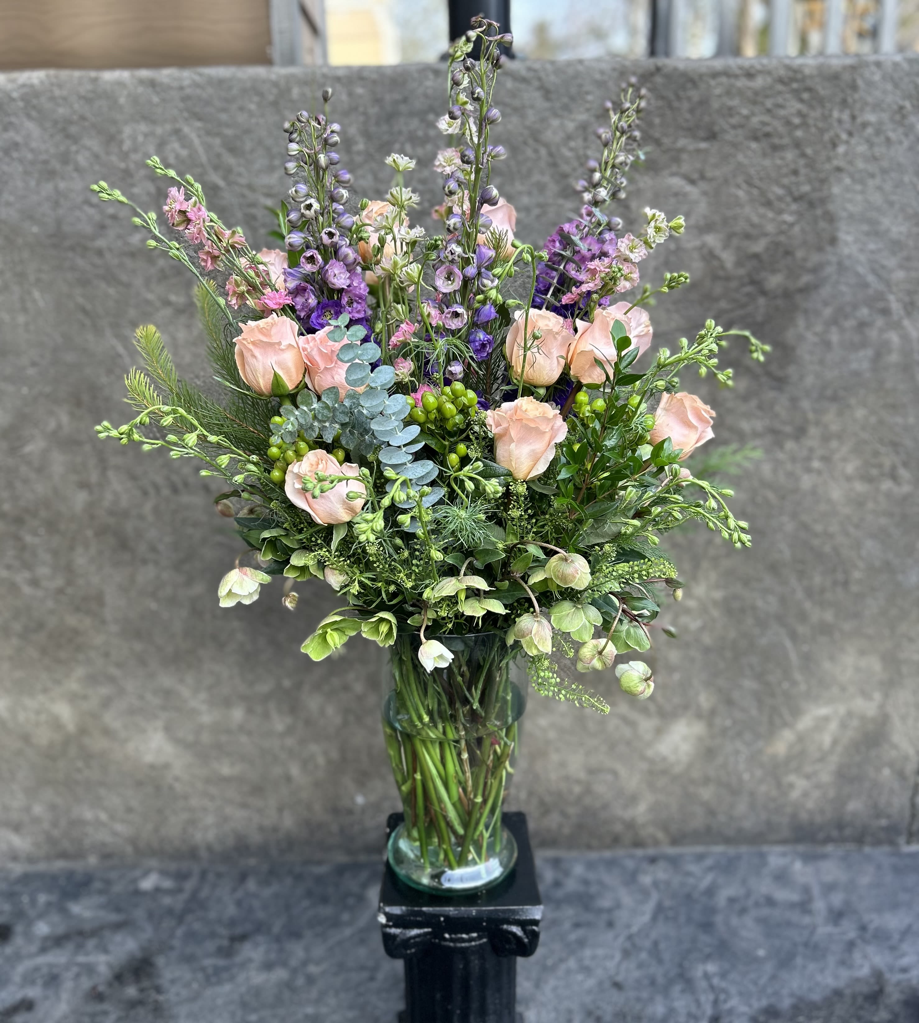 Tall bouquet of blush roses and purple flowers in a glass vase