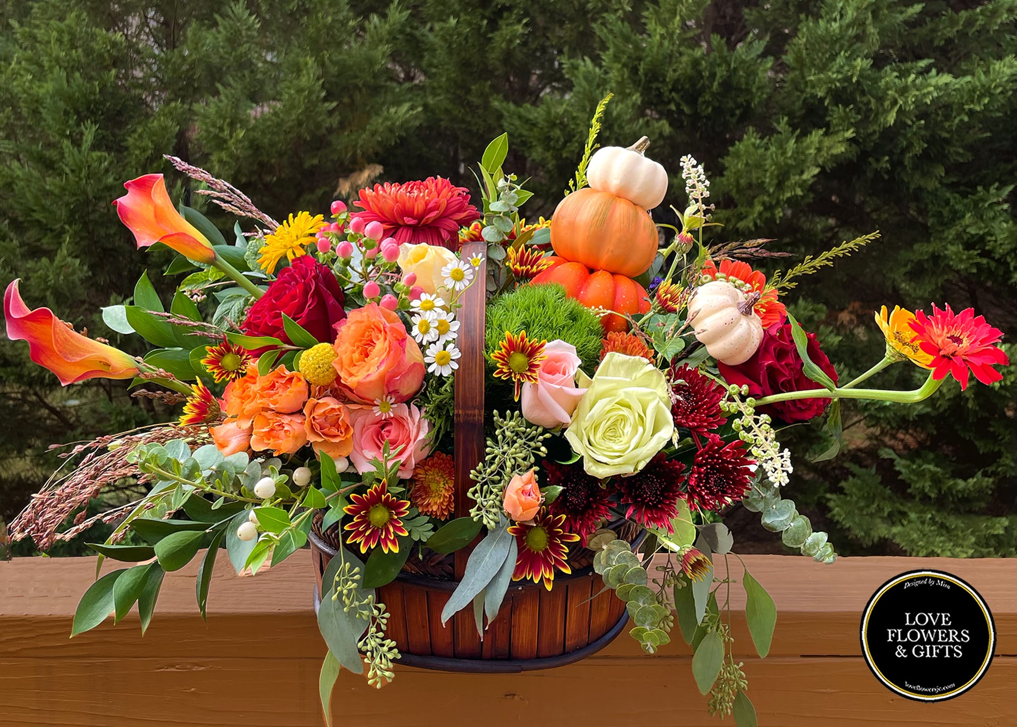 Autumn basket arrangement with orange calla lilies, mixed roses, mums, and mini pumpkins